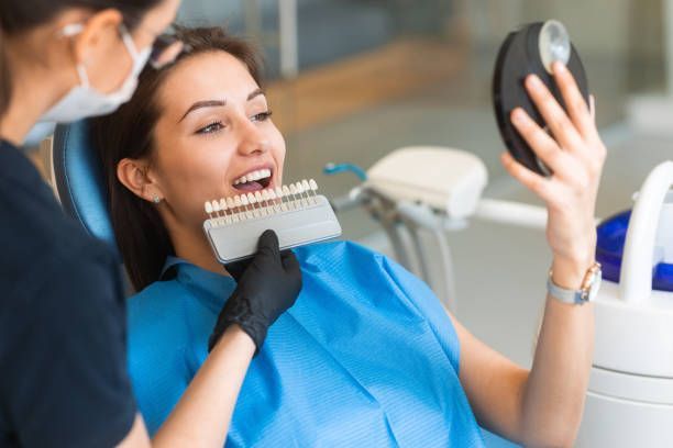 A dentist uses a tooth shade guide to match color for veneers during a cosmetic dentistry consult.