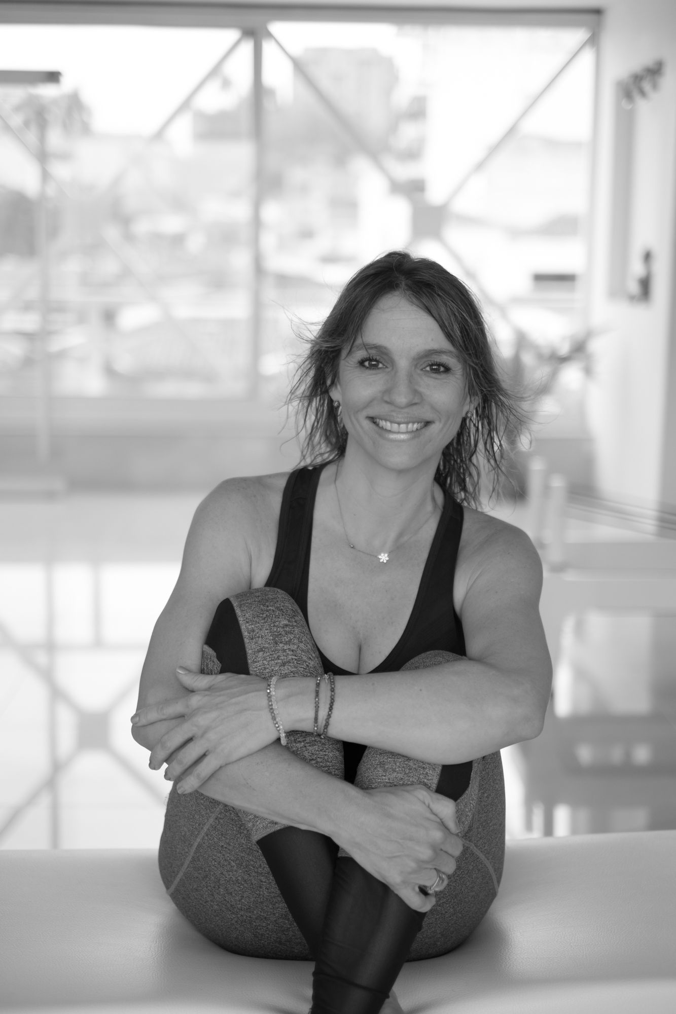 Una mujer está sentada en una mesa con las piernas cruzadas y sonriendo.