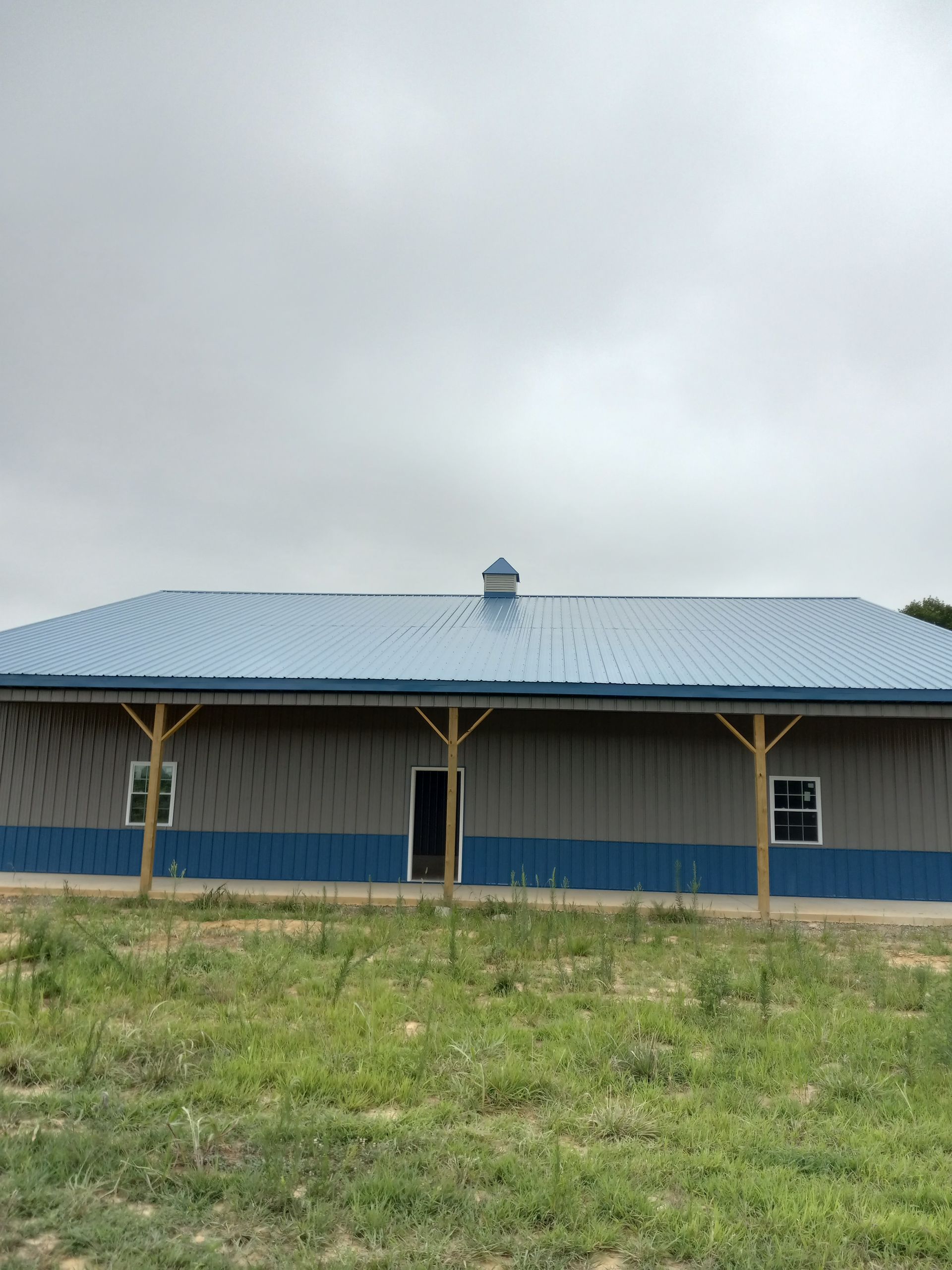 A large building with a blue roof is sitting in the middle of a grassy field.