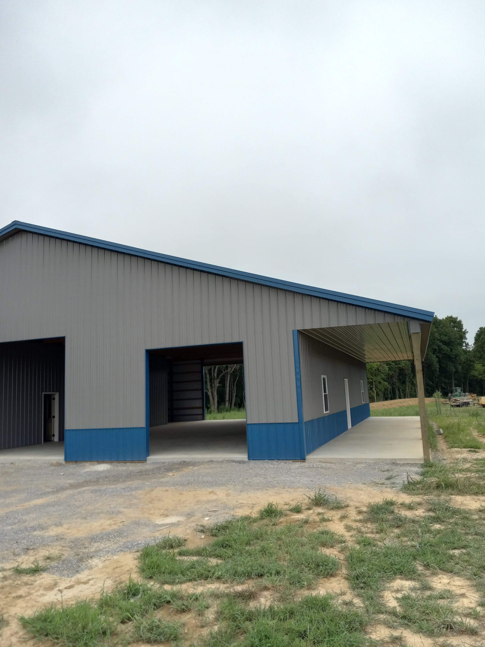 A gray and blue building with a blue roof is in the middle of a grassy field.