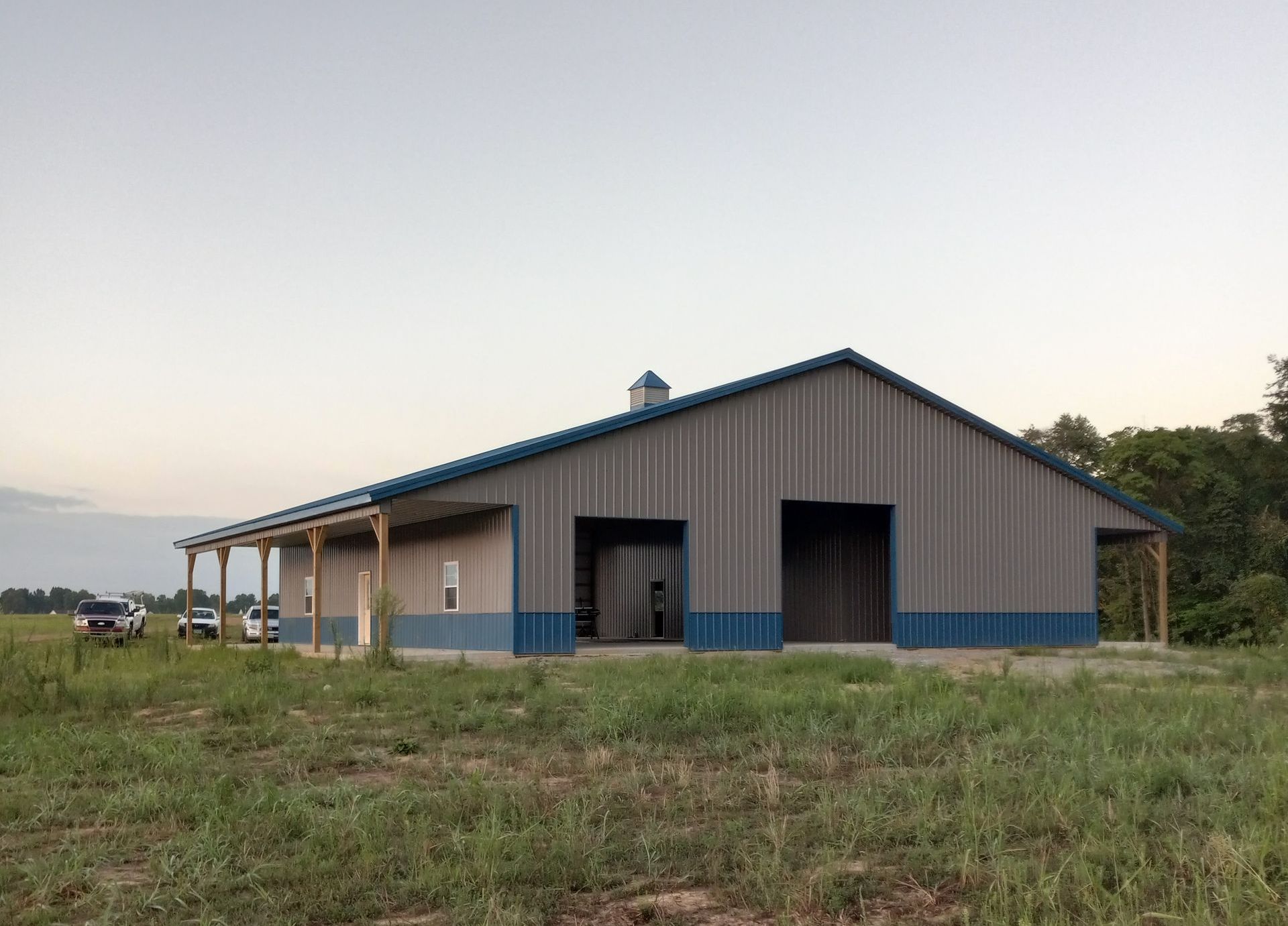 A large building with a blue roof is sitting in the middle of a grassy field.