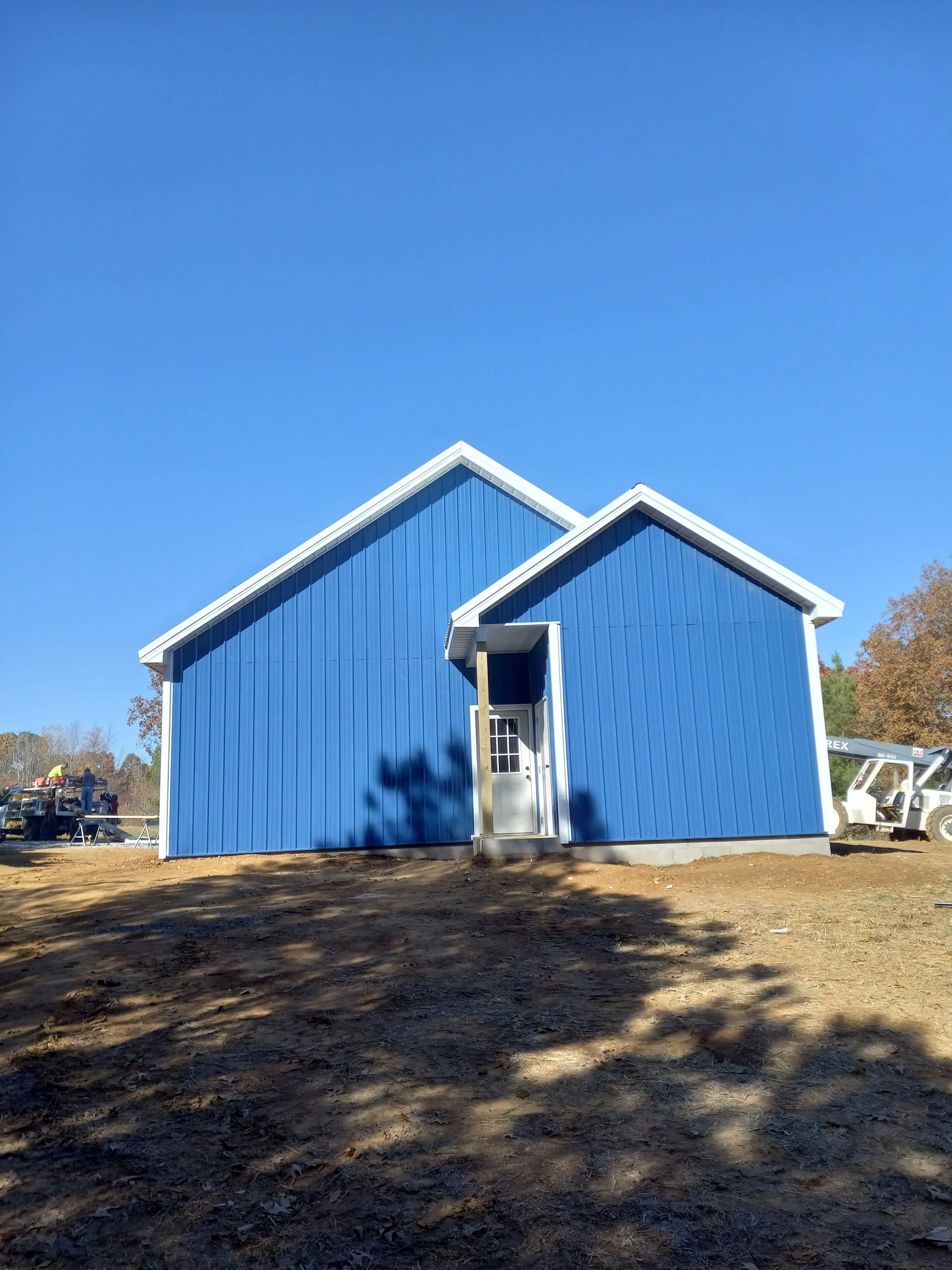 A blue house with a white roof is sitting in the middle of a dirt field.