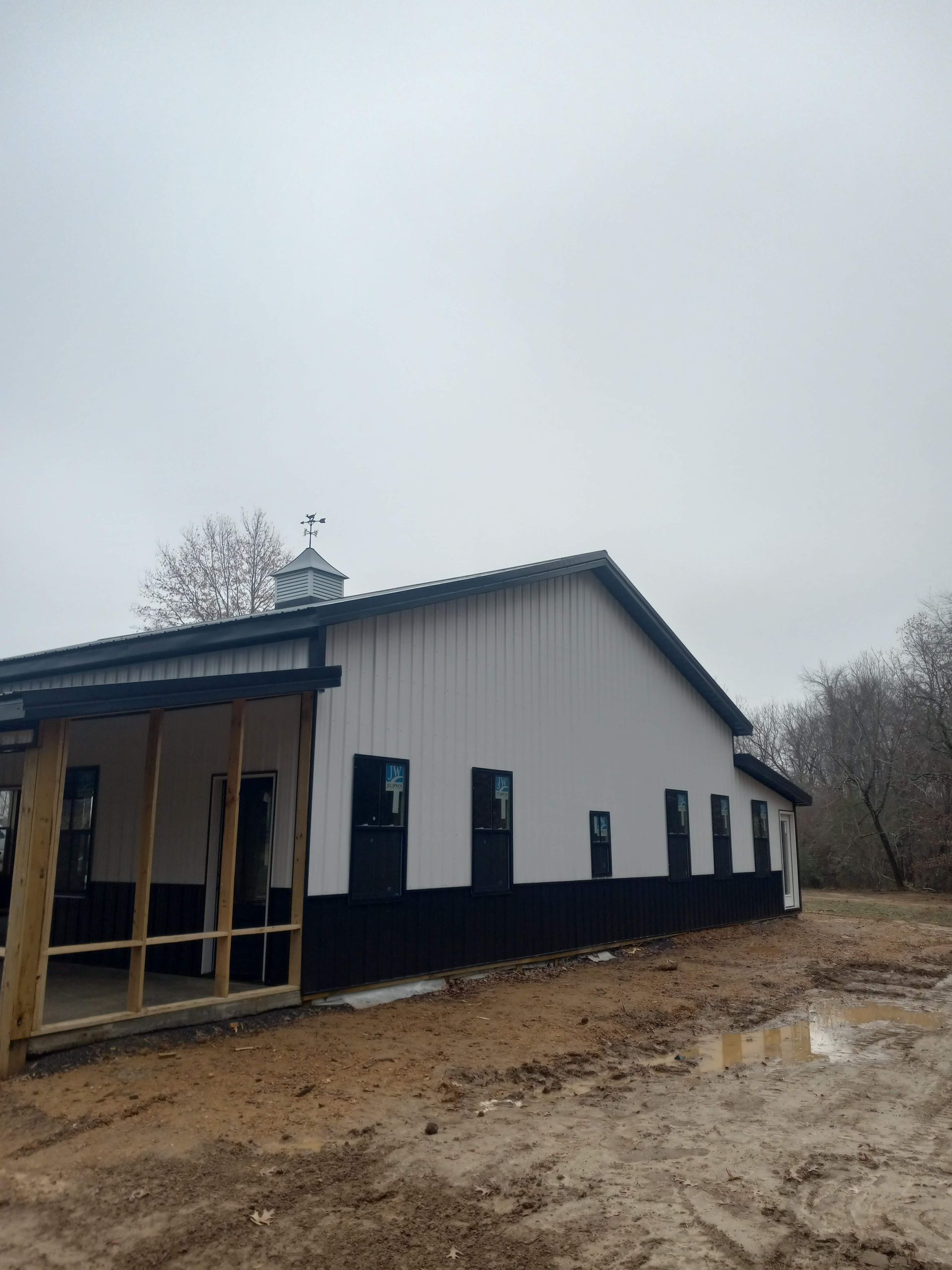 A white and black building with a porch in the middle of a dirt field.