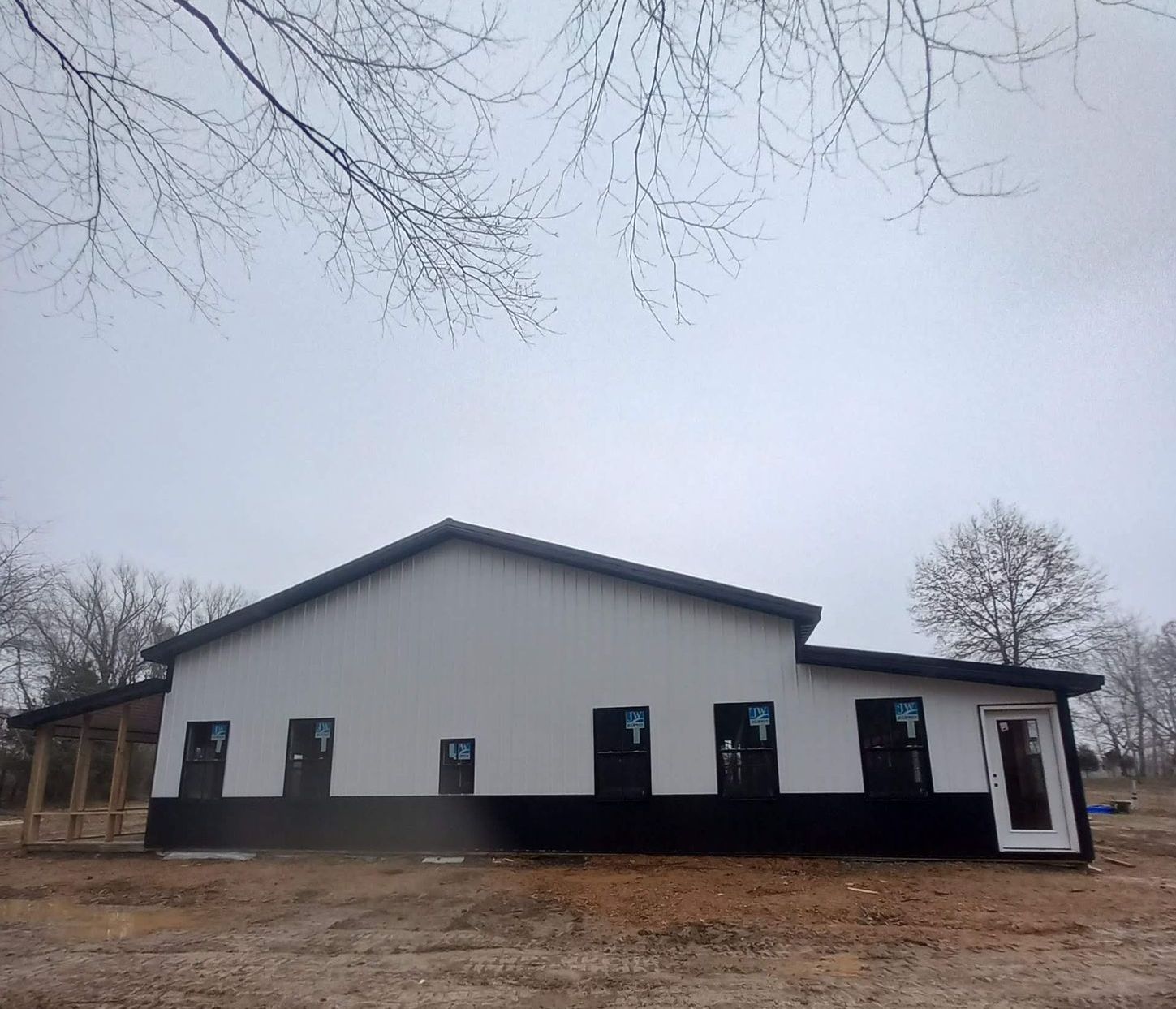 A large white building with black trim is sitting in the middle of a dirt field.