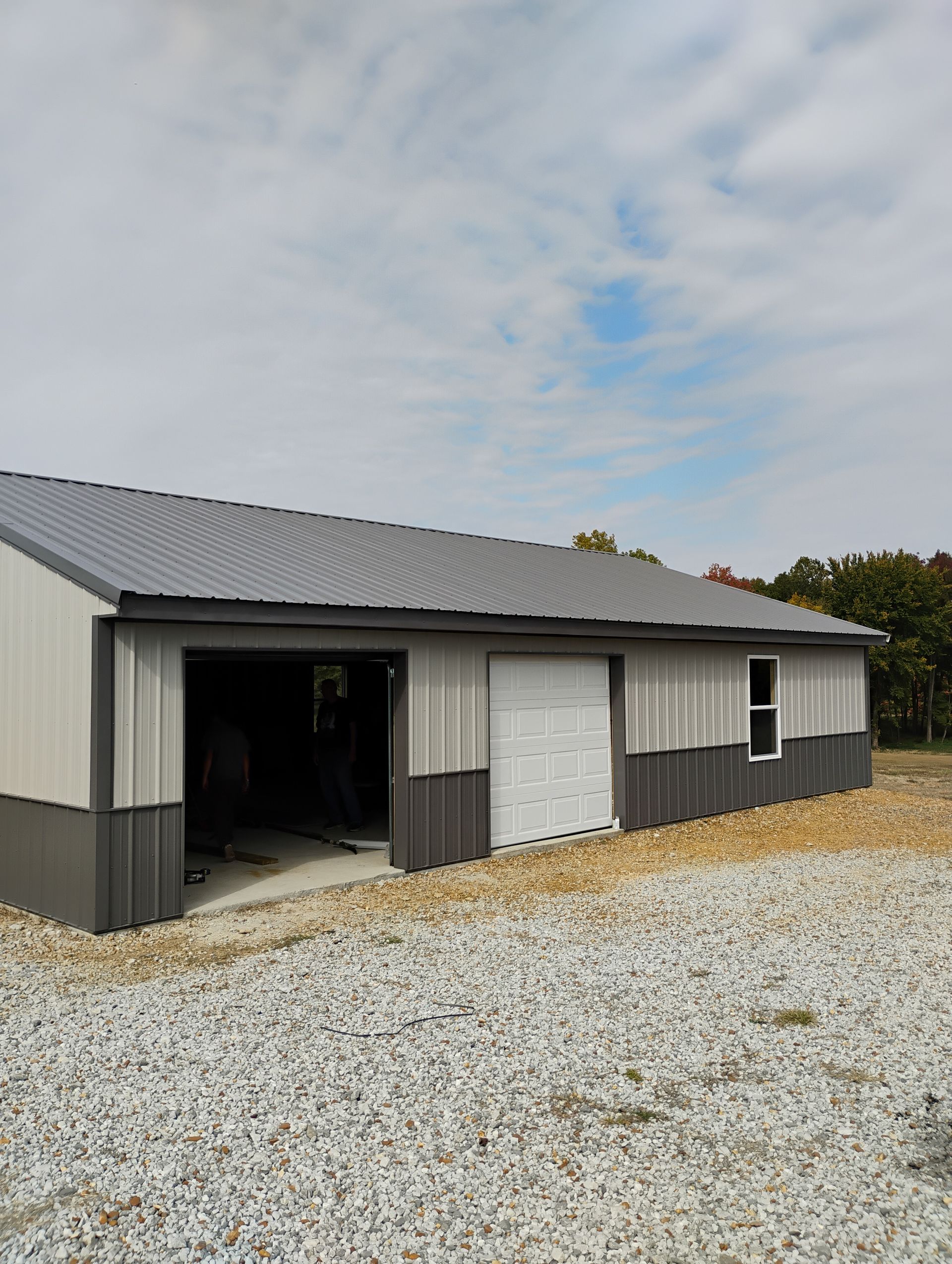 A large metal building with a garage door is sitting on top of a gravel lot.