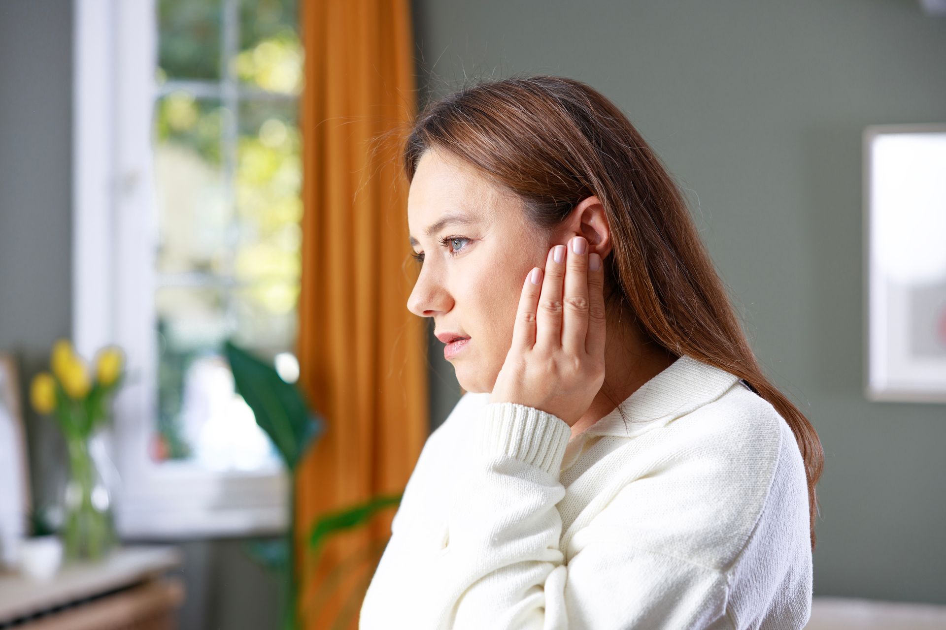 A young woman holding her left ear with ear pain at home. A young woman holding her left ear with ear pain at home.