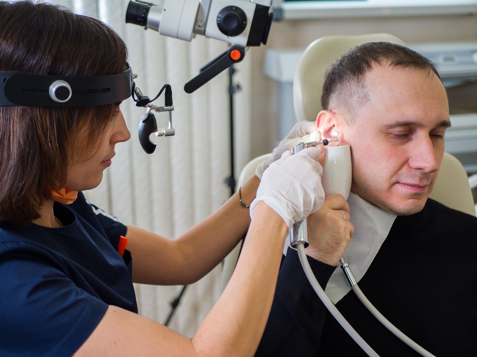 A doctor is performing a micro-ear cleaning on a male patient at a clinic.
