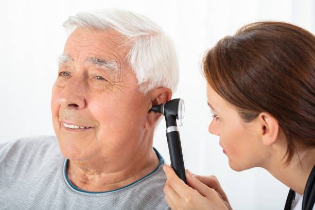 Healthcare professional performing ear examination with otoscope on senior patient in clinic.