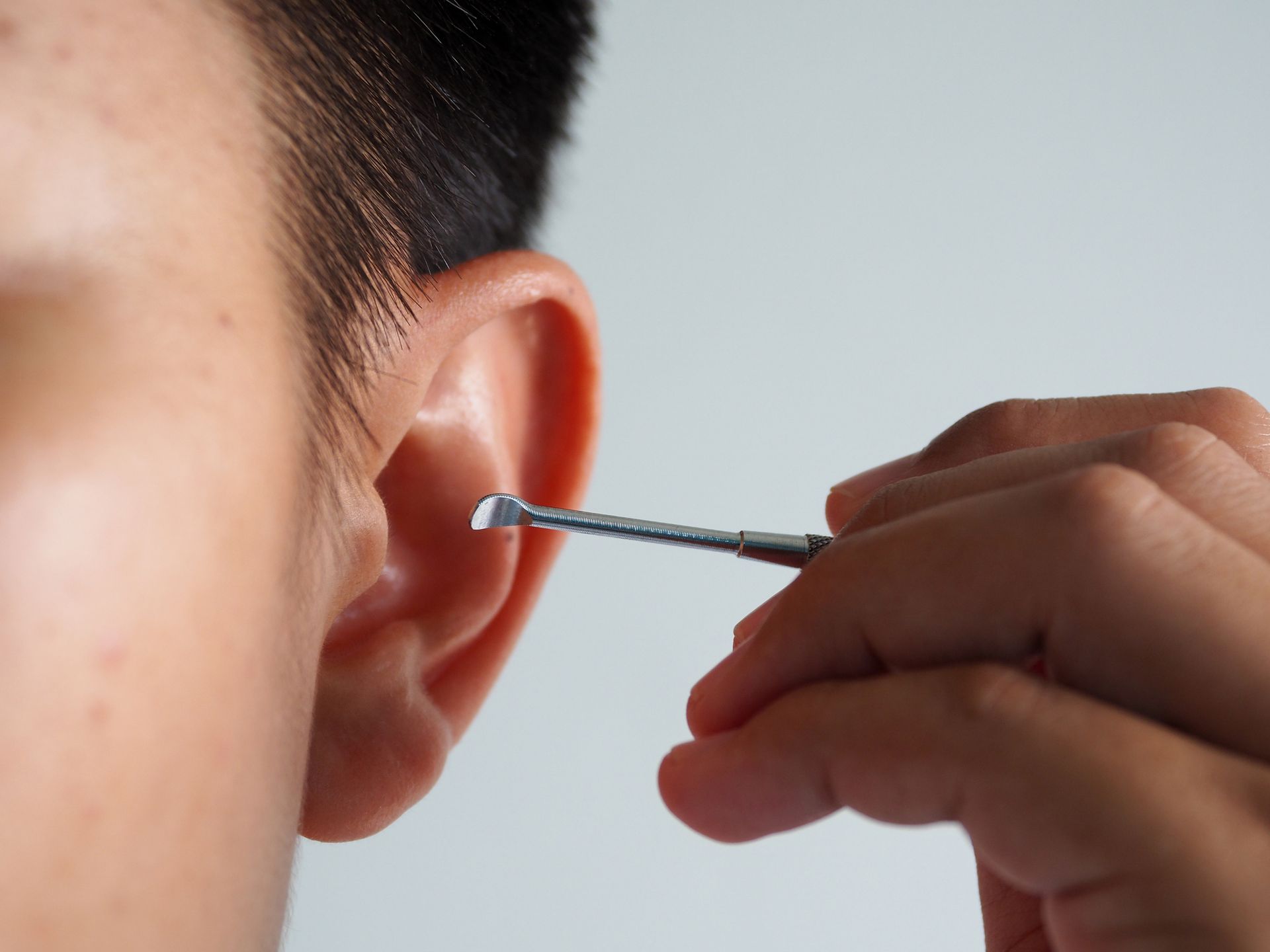Close-up of ear being cleaned with a small metal tool held by a person's hand. Close-up of ear being cleaned with a small metal tool held by a person's hand.