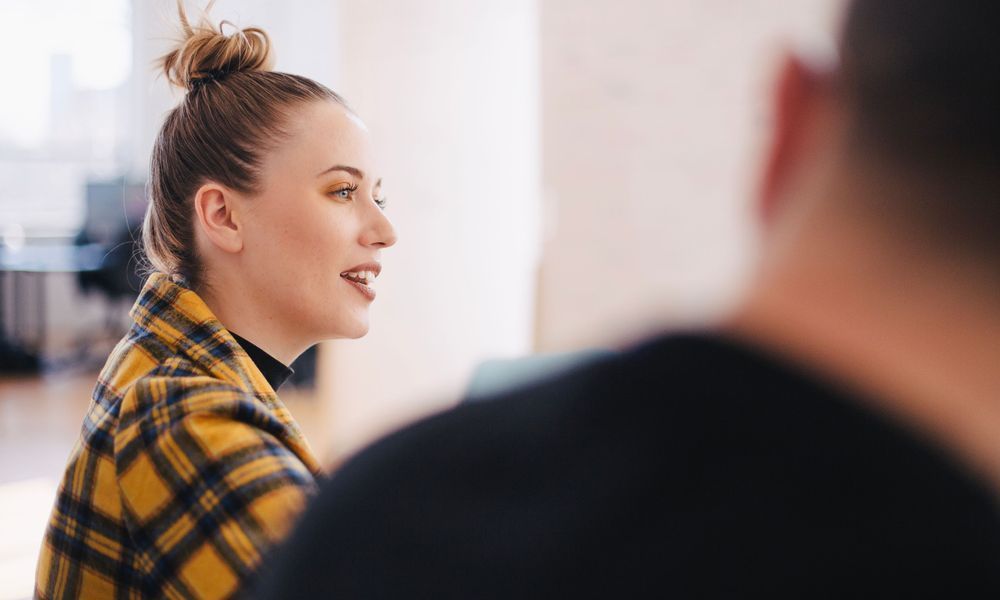 A woman in a plaid coat is talking to a man in a black shirt.