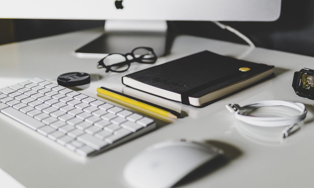 A desk with a computer , keyboard , mouse , notebook , pencil and glasses.