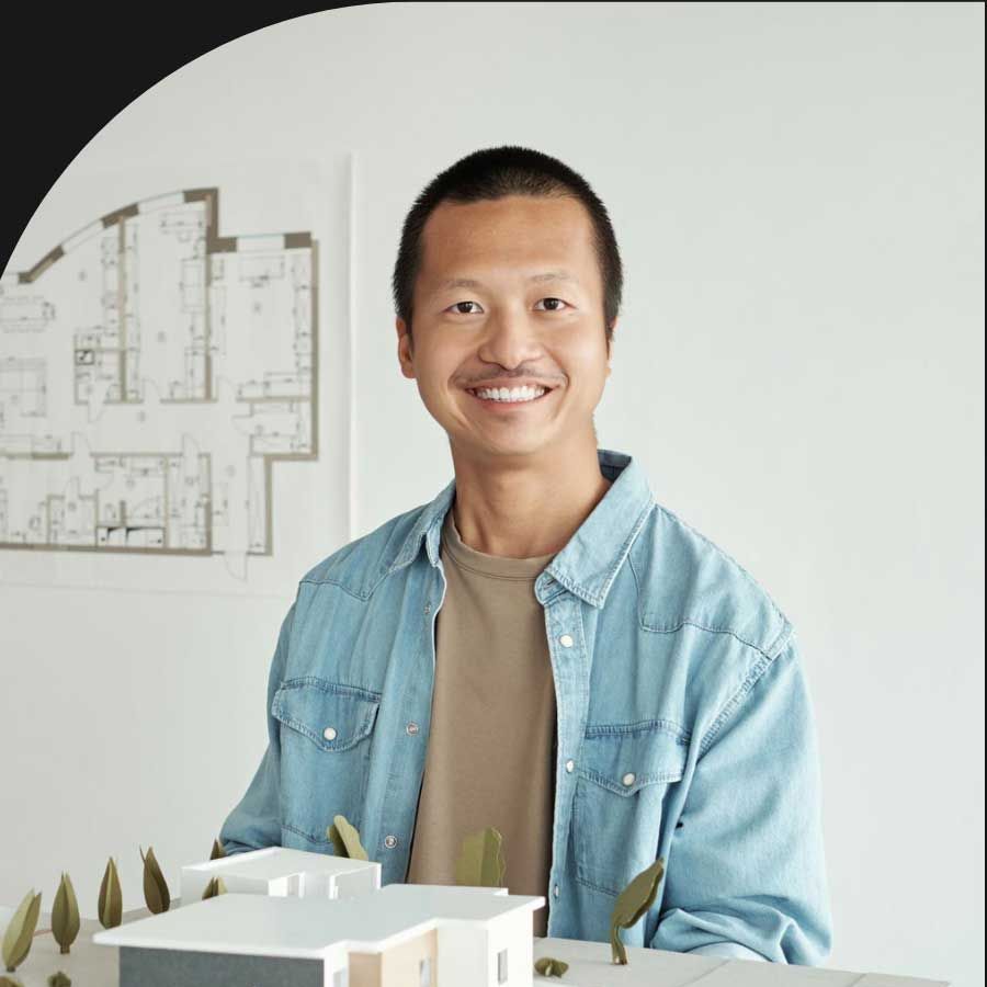 A man in a denim shirt is smiling while holding a model house