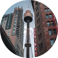 Looking up at a tower between two tall buildings in a city.