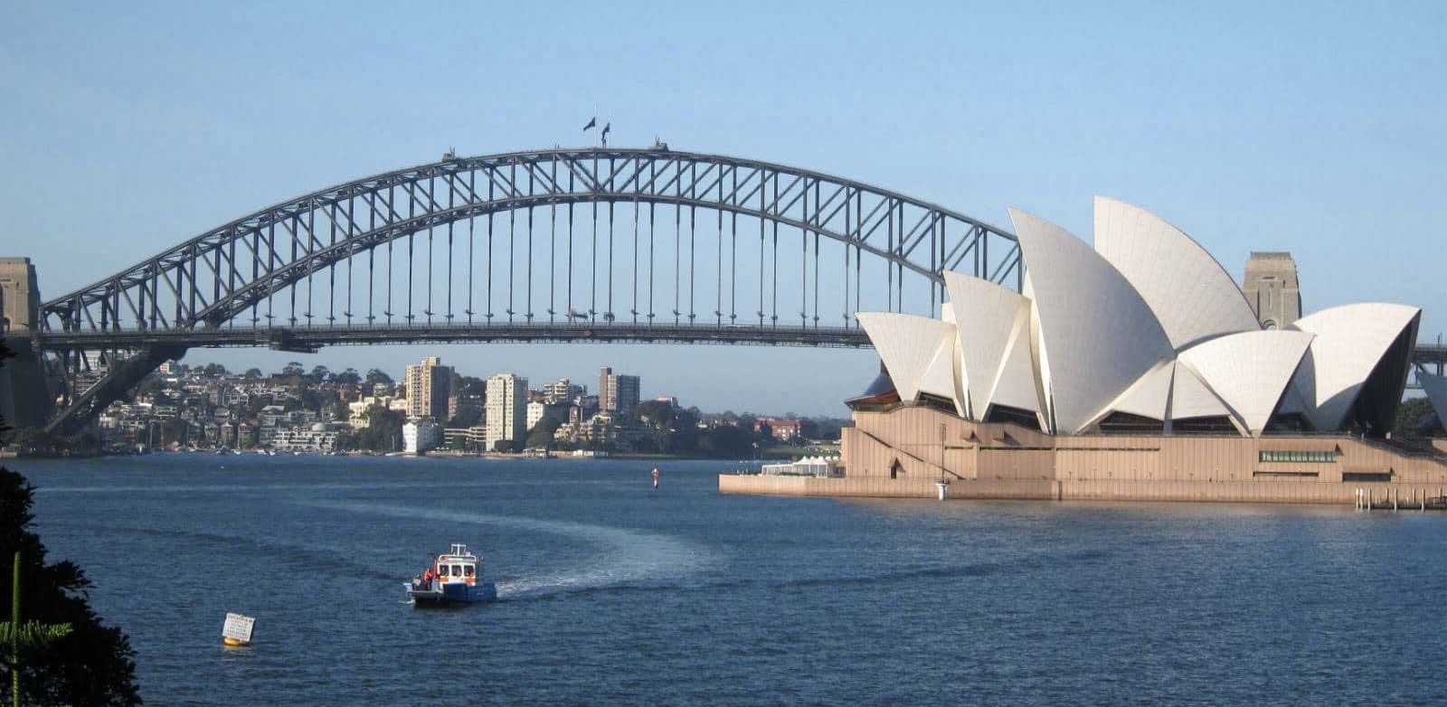 A bridge over a body of water with the opera house in the background