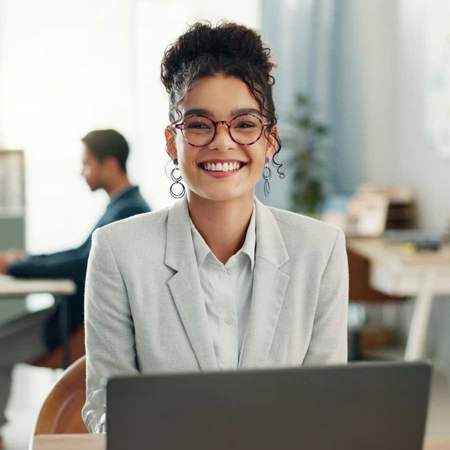 A woman is smiling while sitting in front of a laptop computer.