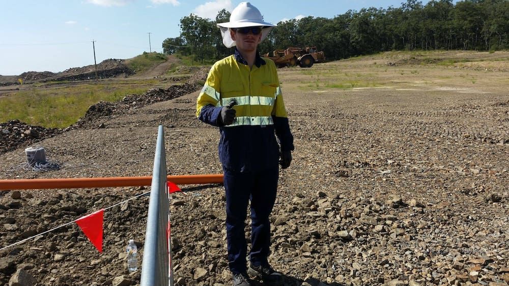 A Man in a Hard Hat and Safety Vest is Standing in a Dirt Field — D.J. Whatley & Son Pty Ltd in Ormeau Hills, QLD