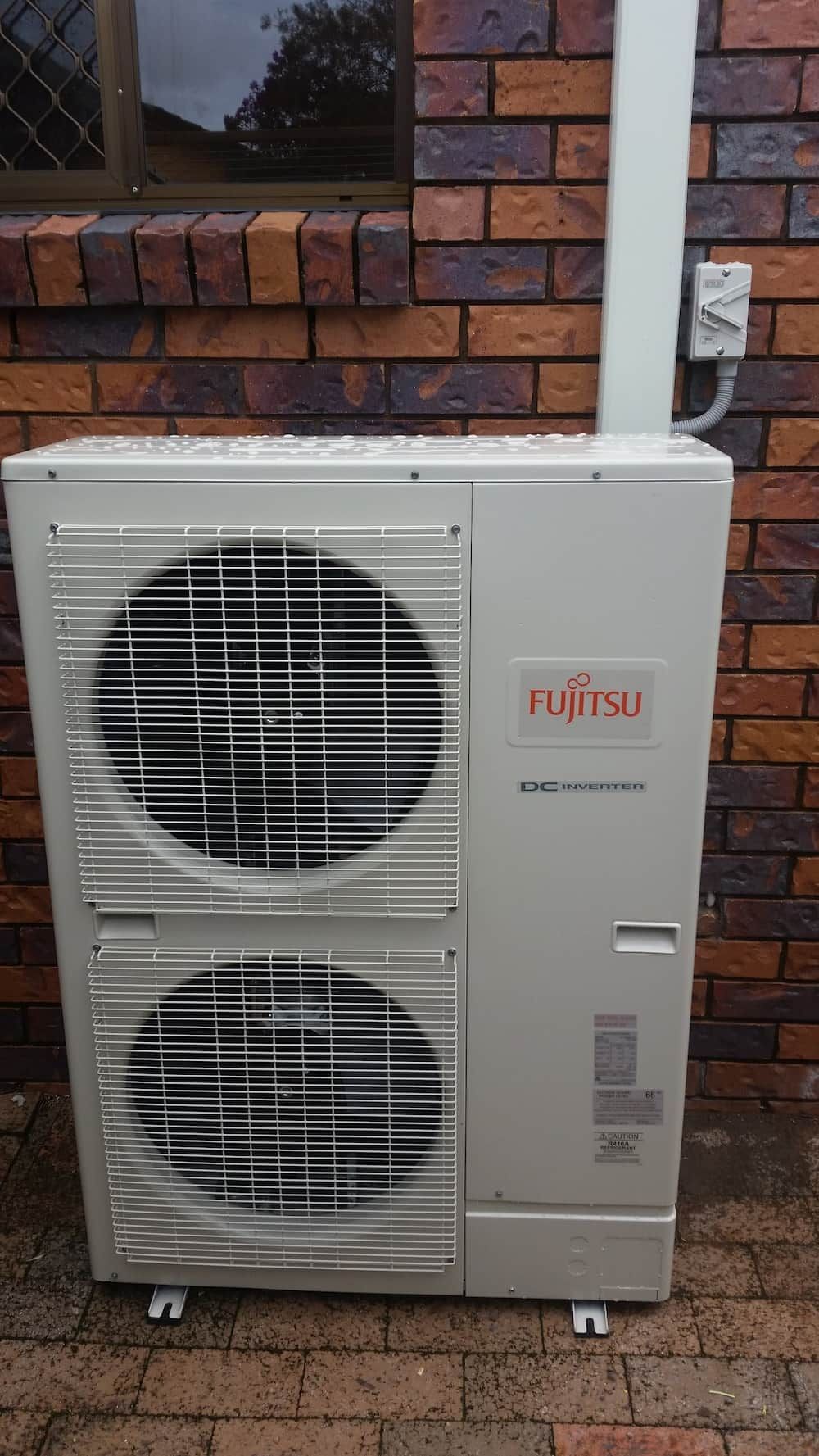 A Fujitsu Air Conditioner is Sitting on the Side of a Brick Building — D.J. Whatley & Son Pty Ltd in Ormeau Hills, QLD