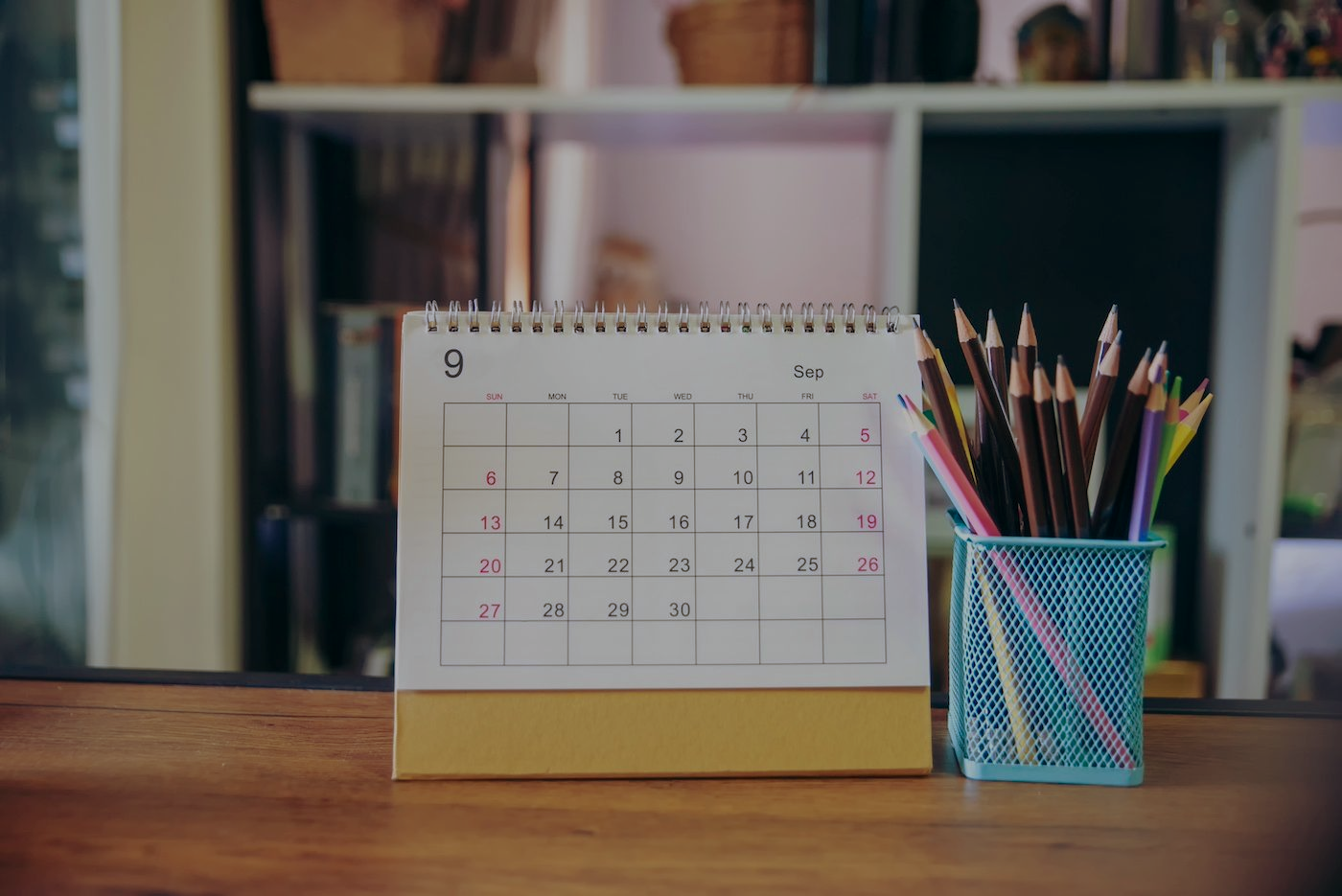 Desk calendar showing the month of September with pencils in a blue holder.