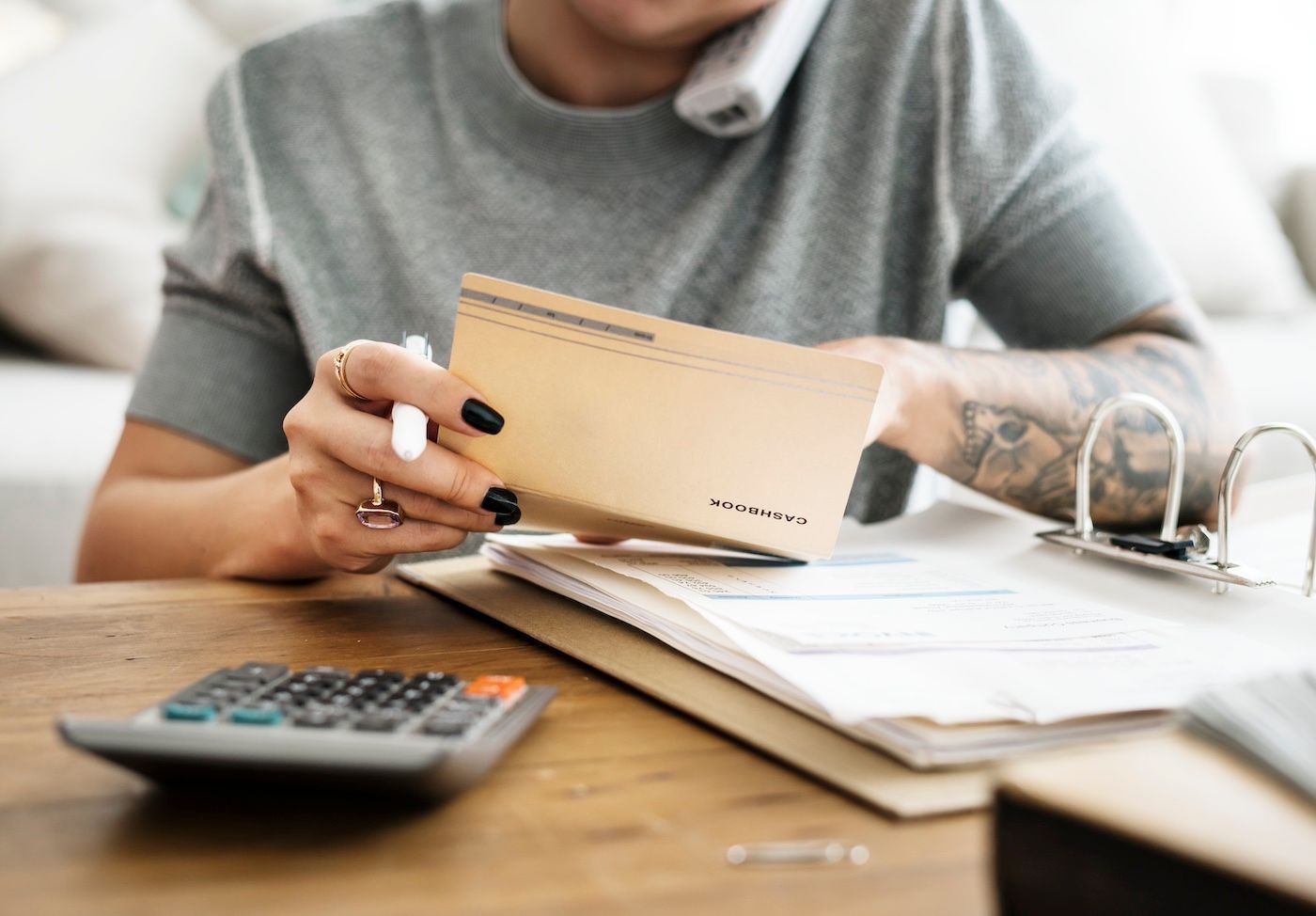Person with tattoo holding envelope over paperwork at a desk with calculator.