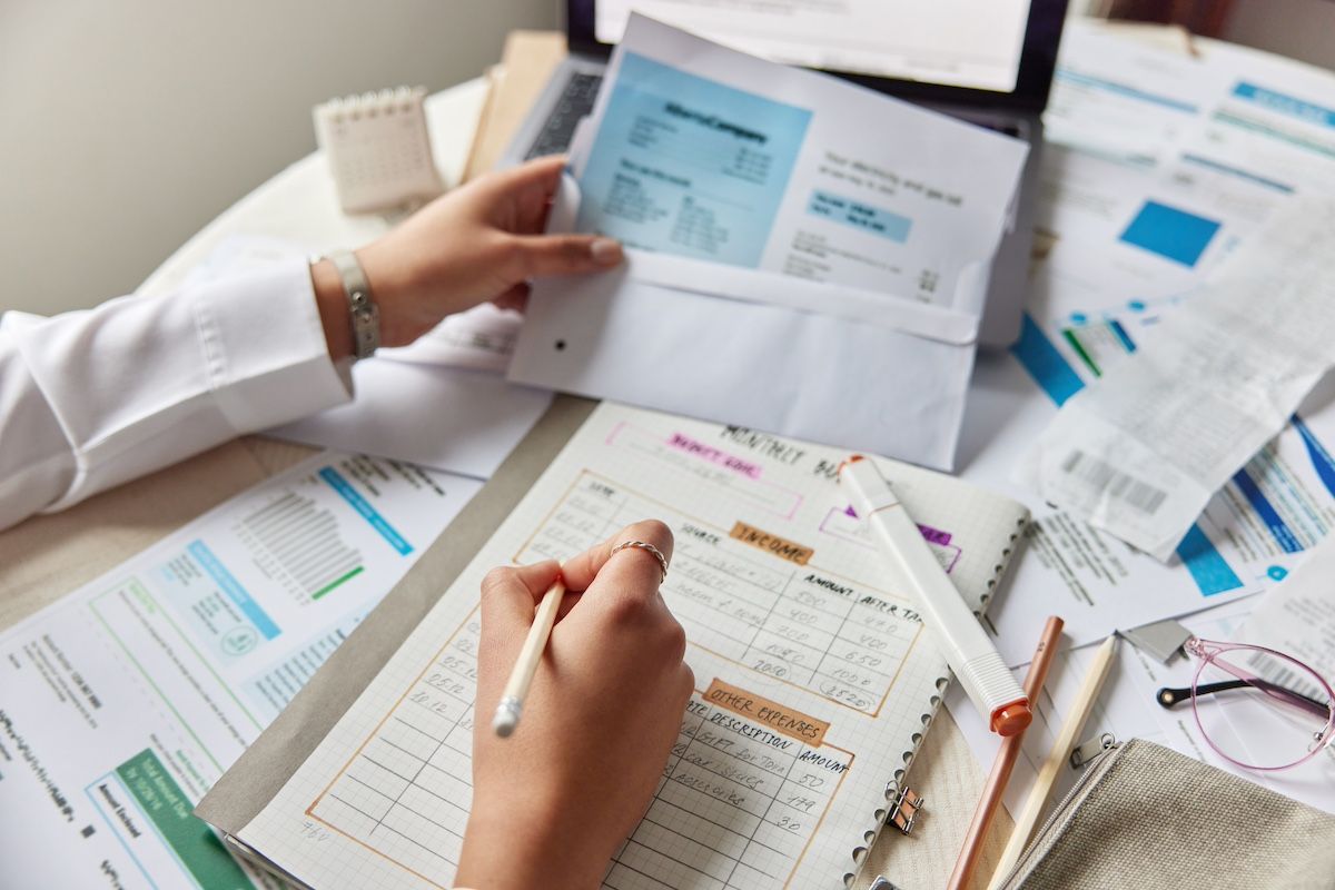 A Woman’s Hand Holds a Hospital Bill Over a Deck Full of Other Bills. Call Duckworth Injury Law.