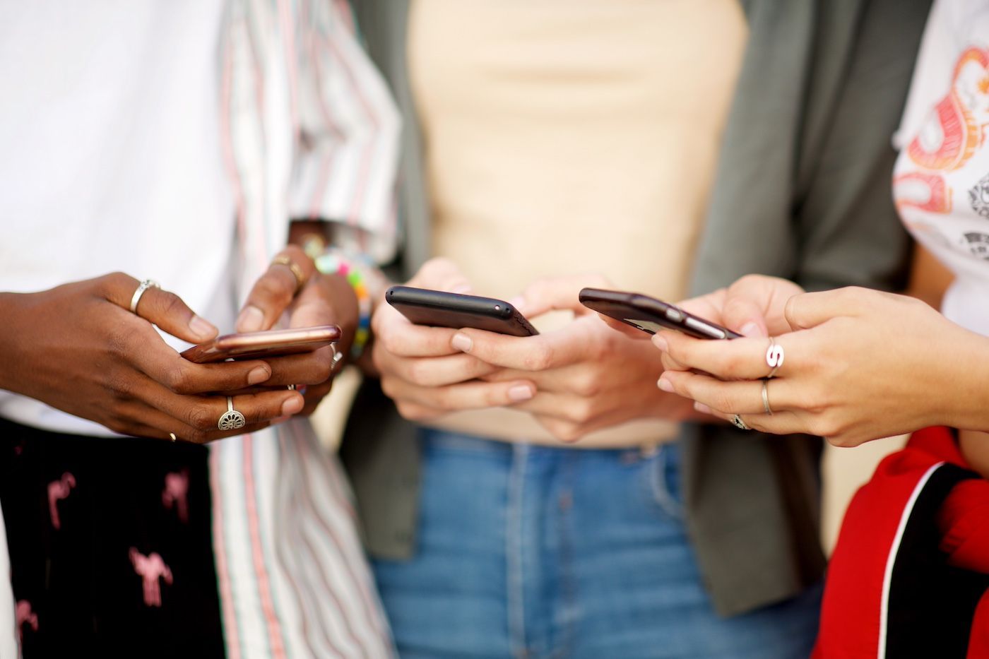 Three people stand together, each using a smartphone in their hands.