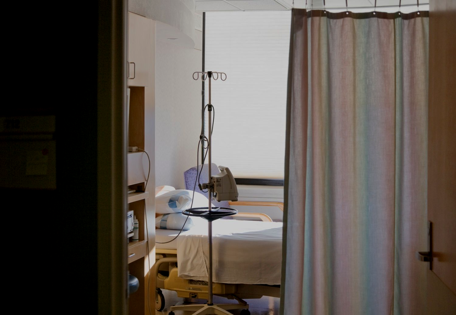 A hospital room with an emptybed and partially drawn curtains. 