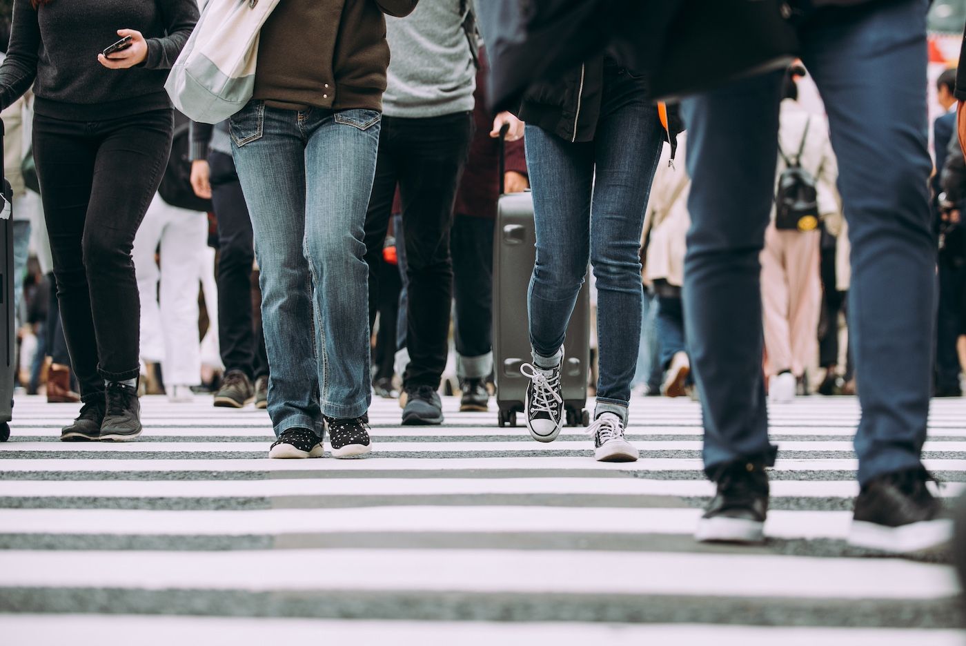 A low-angle view of multiple people walking across a white and gray striped pedestrian crosswalk.