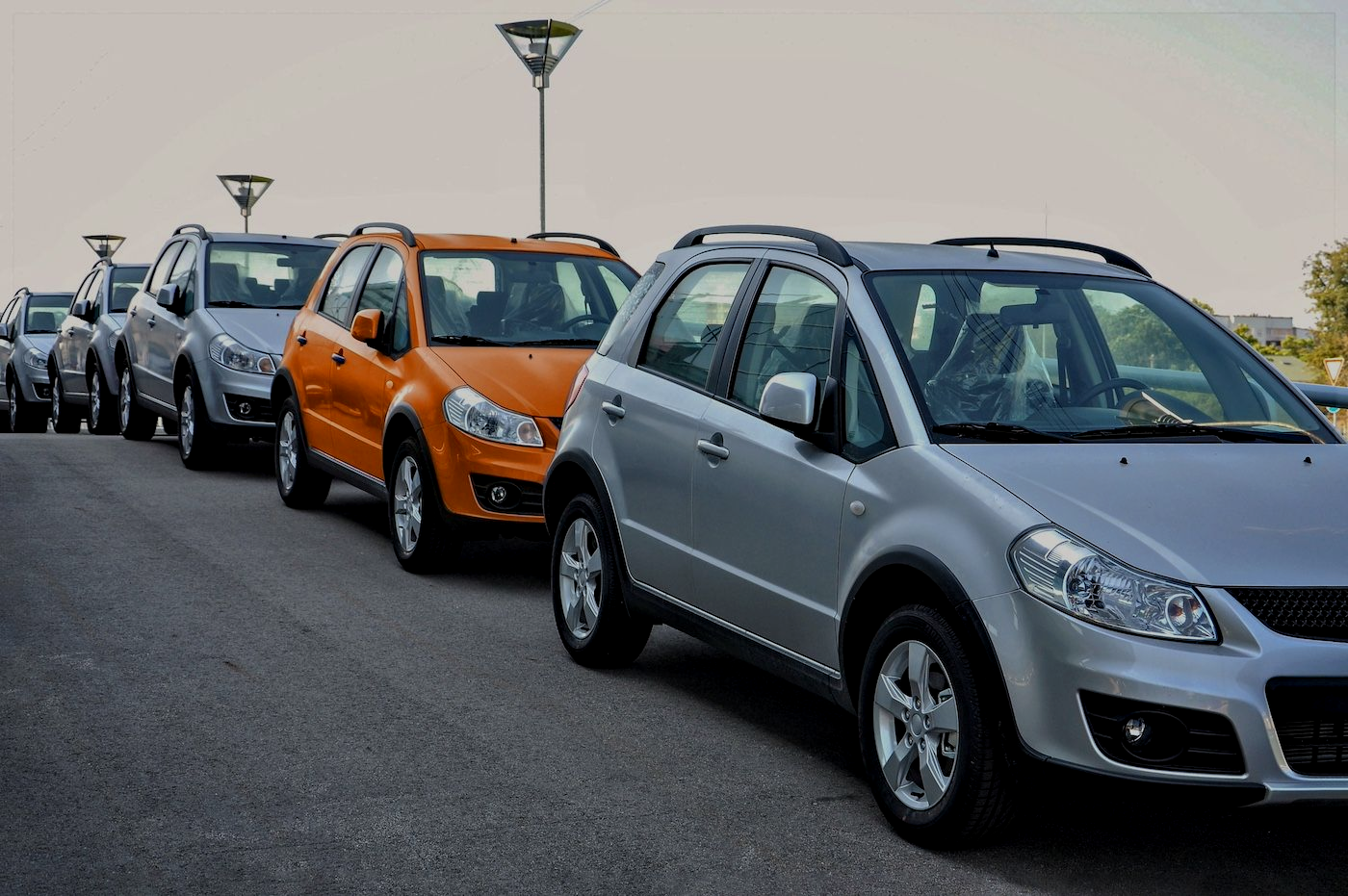 Cars parked in a line, silver, orange, and gray, outdoors.