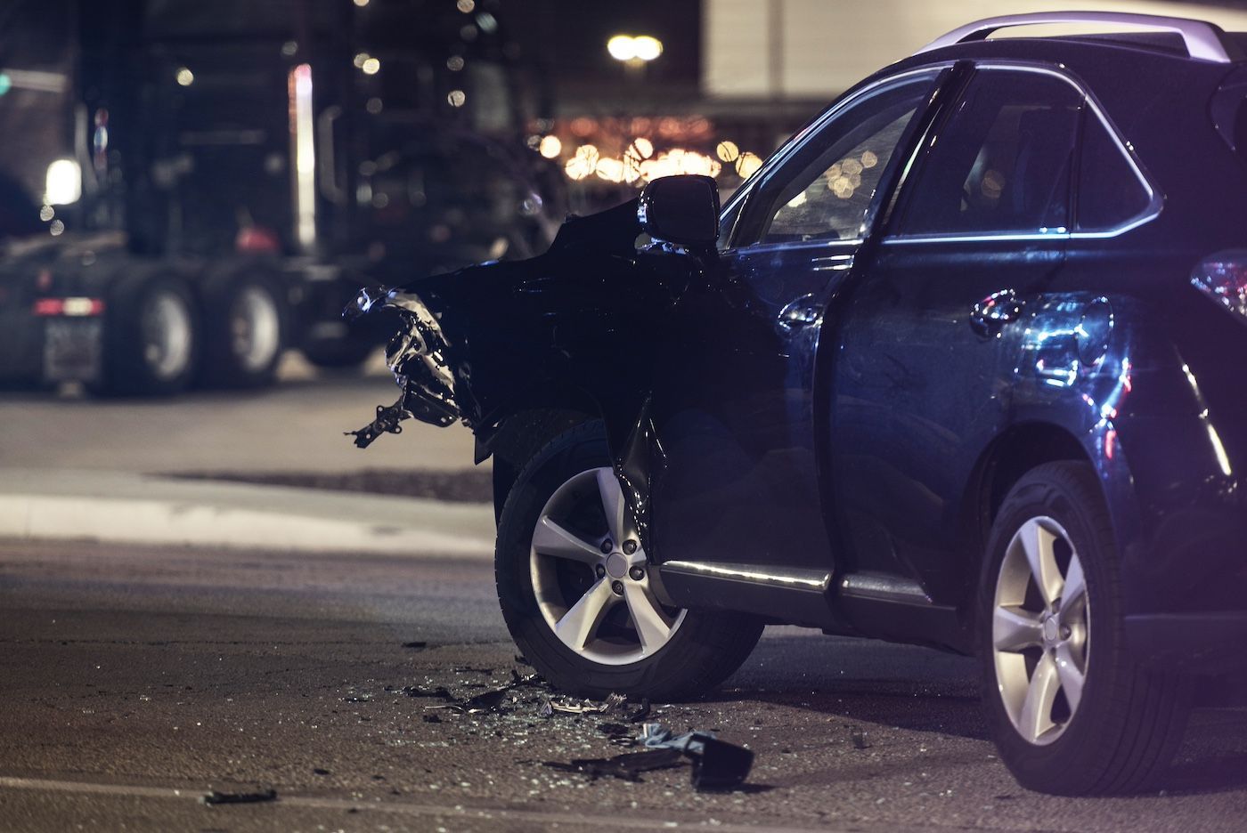 Damaged blue SUV after a nighttime collision, with front-end debris on the road.