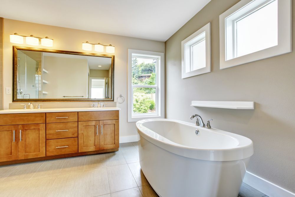 A bathroom with a tub , sink , mirror and two windows.