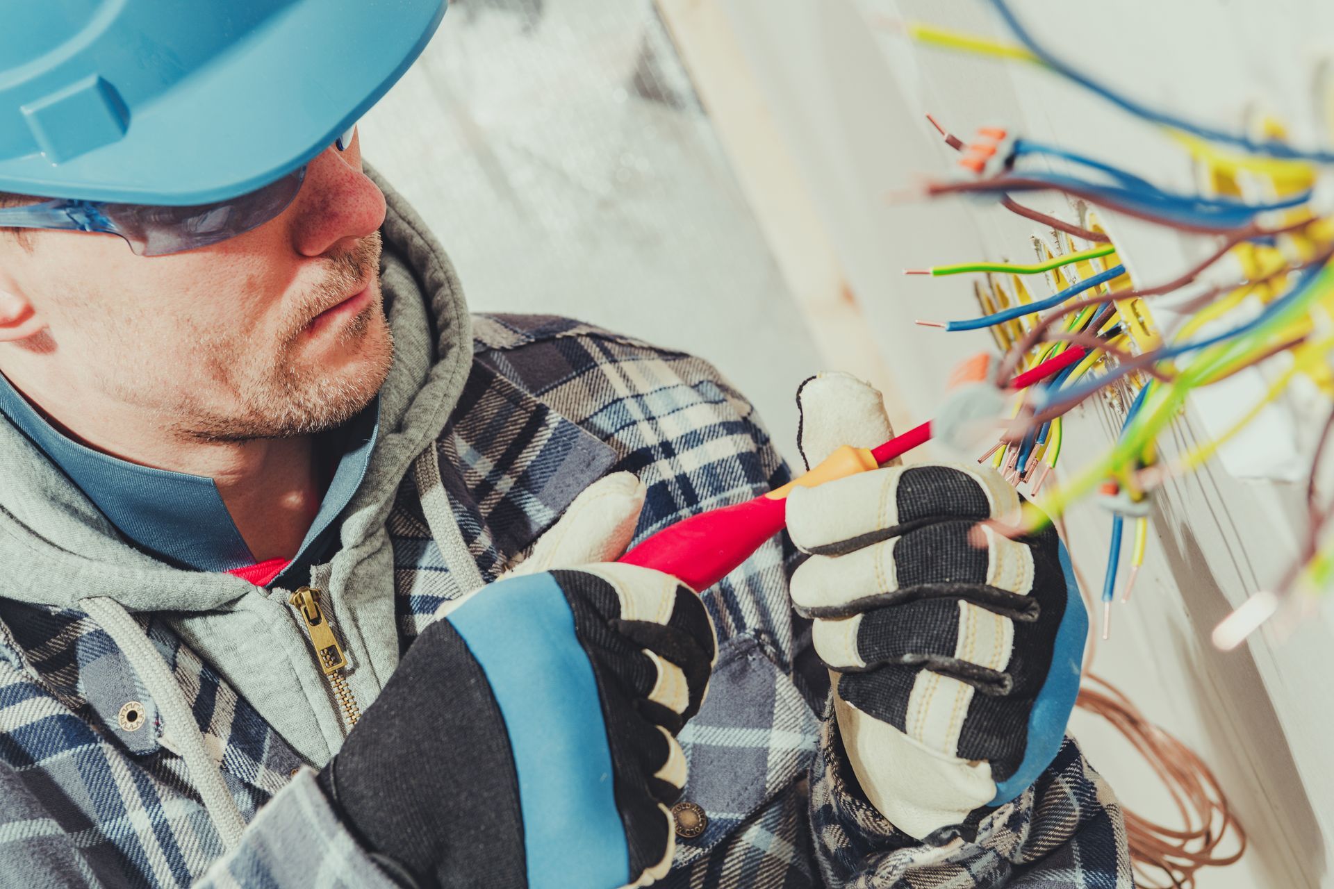 A man wearing a hard hat and gloves is working on electrical wires.
