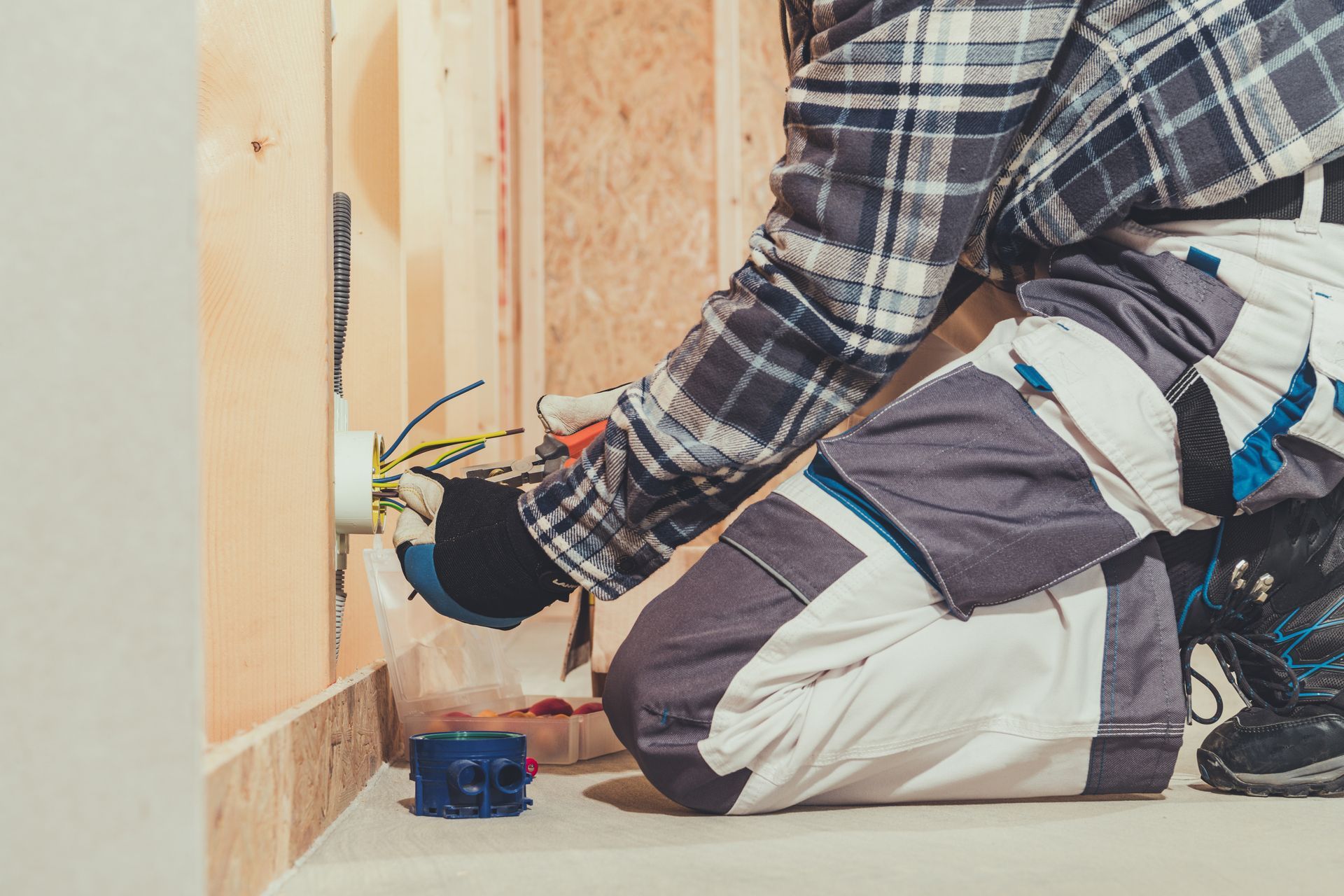 A man is kneeling down and working on an electrical outlet.