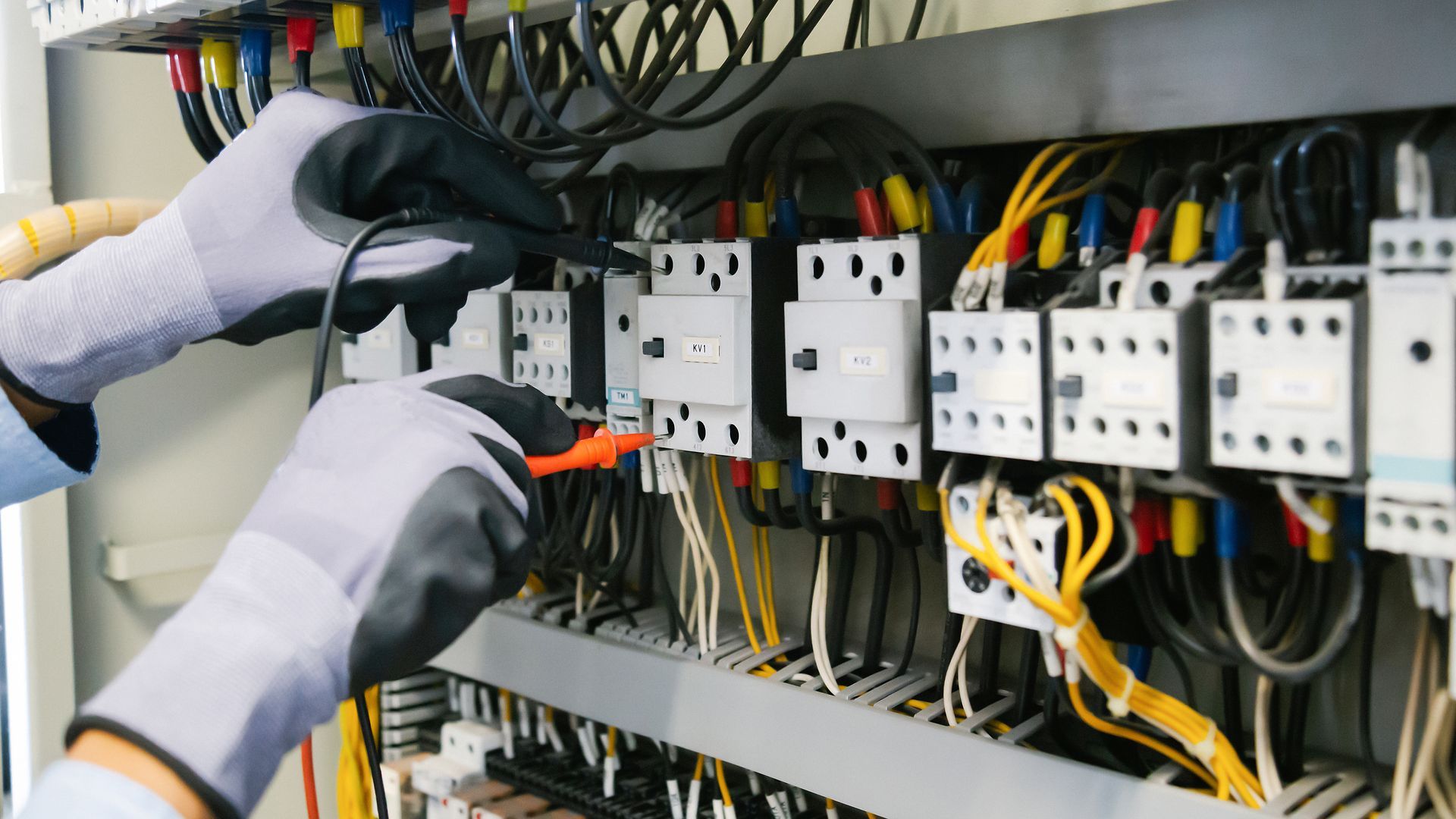 An electrician is working on an electrical panel with a screwdriver.