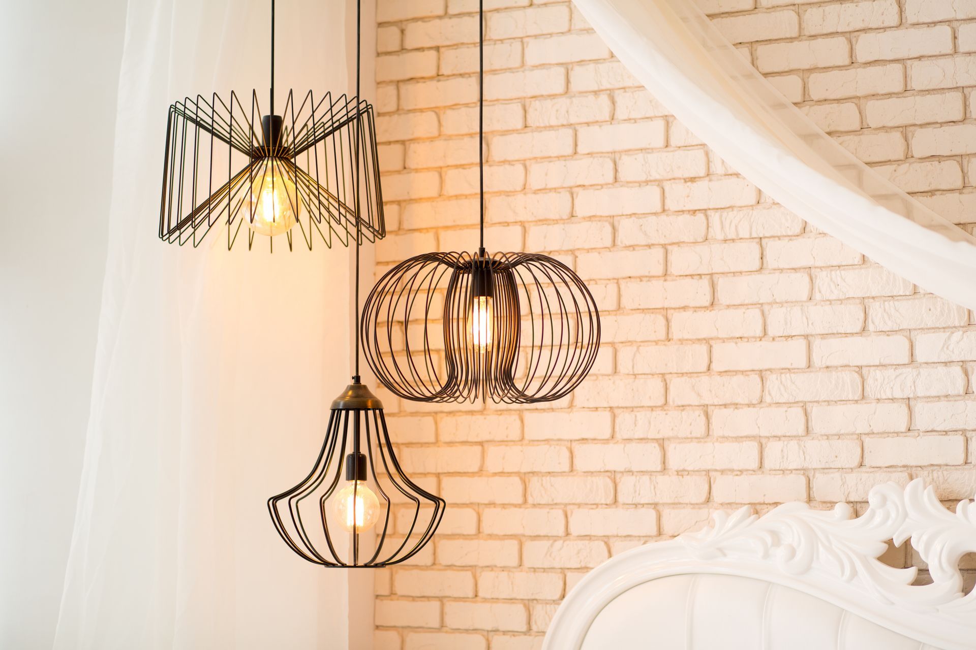 Three pendant lights are hanging from the ceiling in front of a white brick wall.