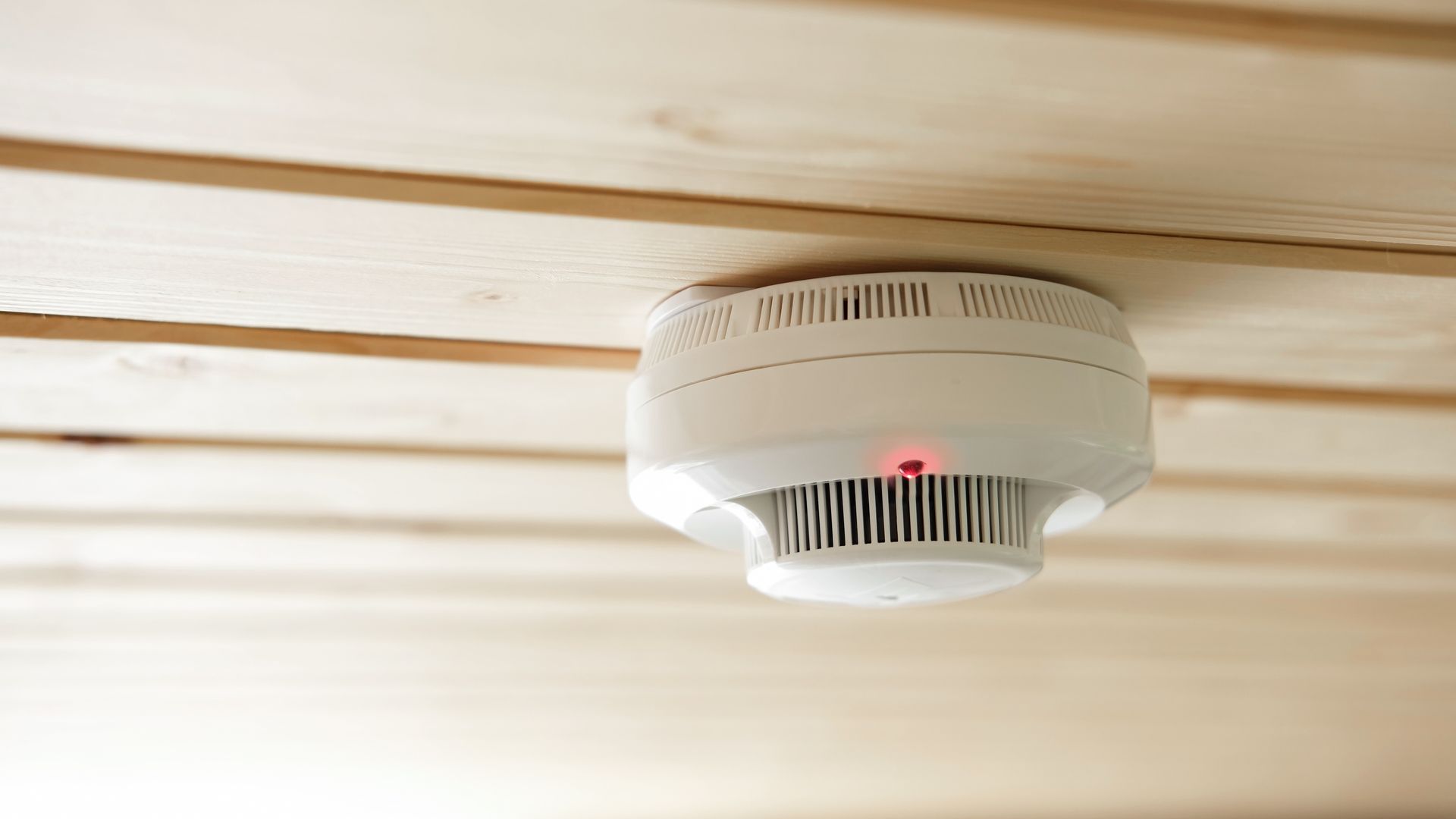 A smoke detector is mounted to the ceiling of a wooden room.
