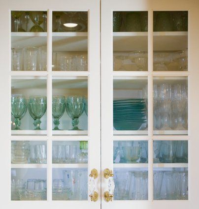 White cabinet doors with glass panes, displaying glassware of various shapes and colors.