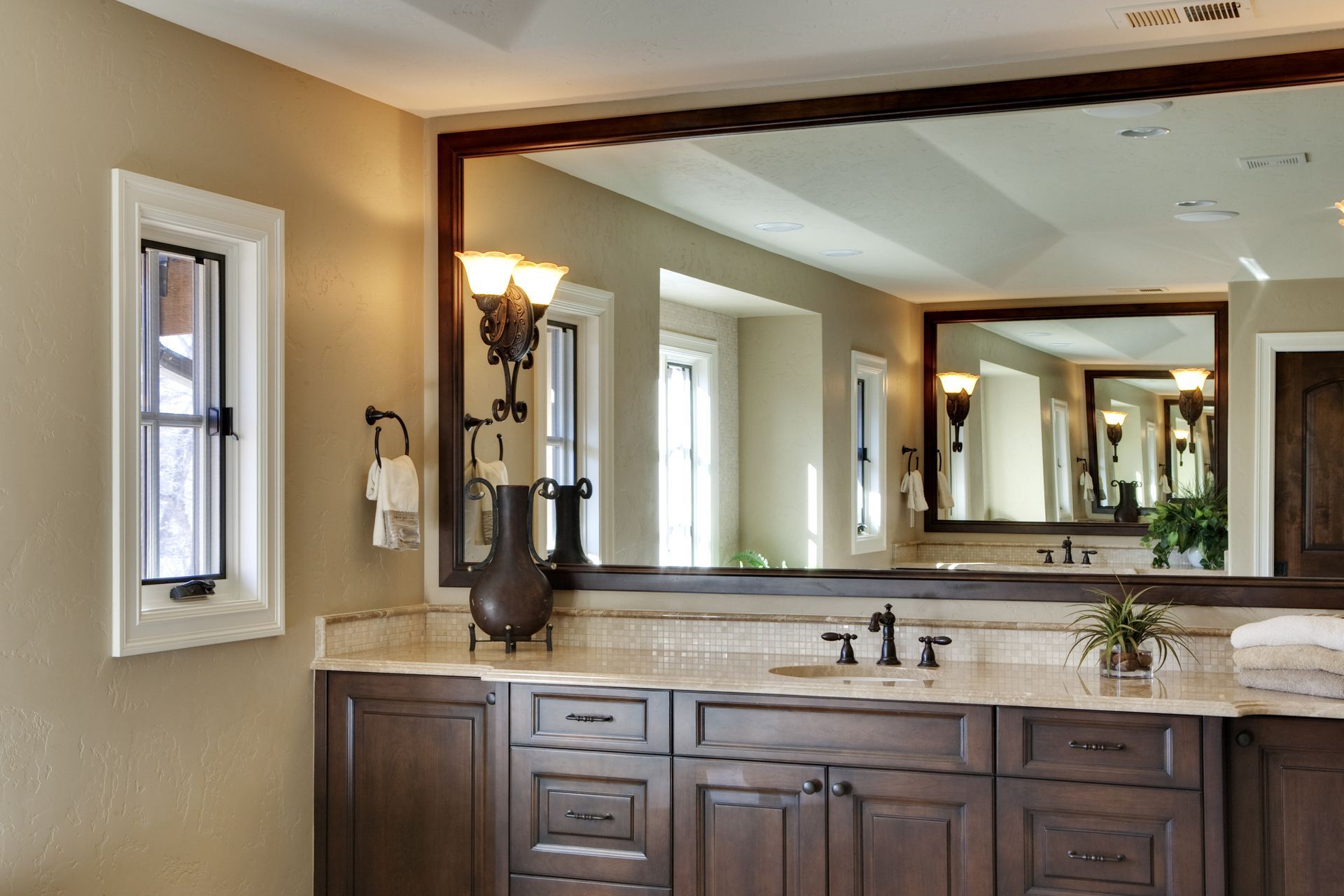 Bathroom with large mirror, dark wood vanity, light countertops, and beige walls.