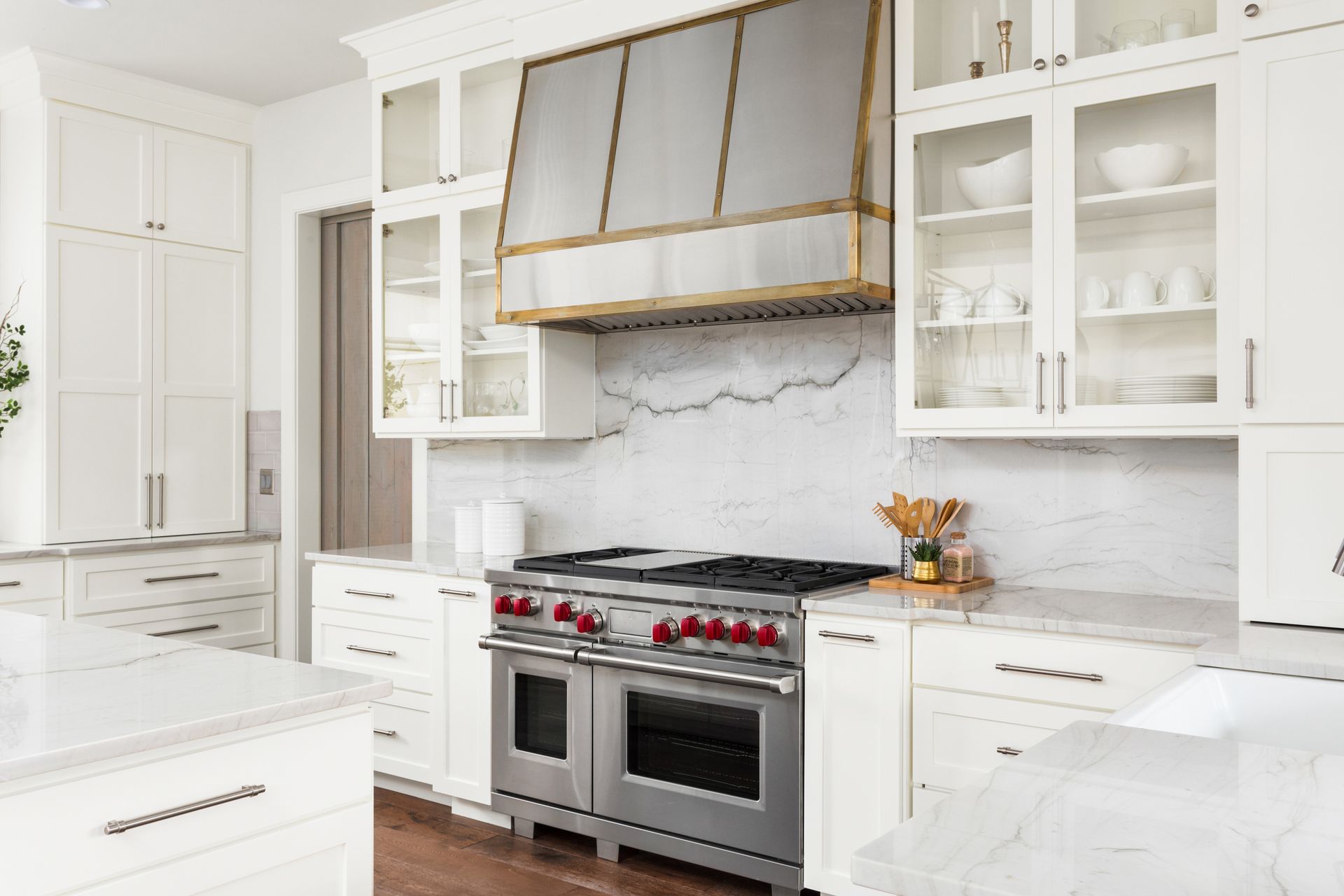 White kitchen with marble countertops, stainless steel appliances, and brass range hood.