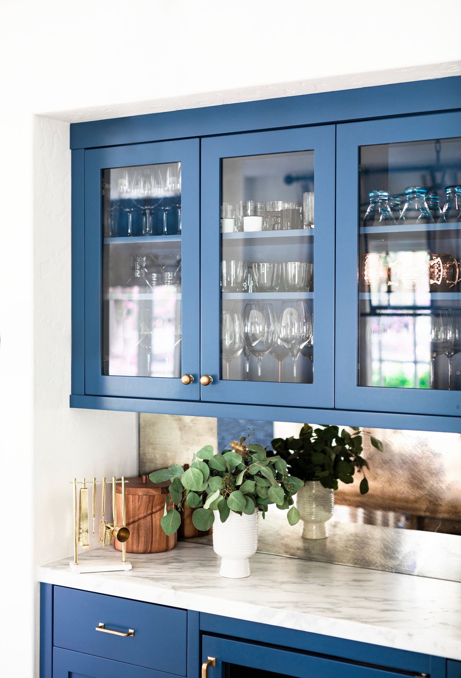 Blue kitchen cabinets with glass doors, displaying glassware. Marble countertop.