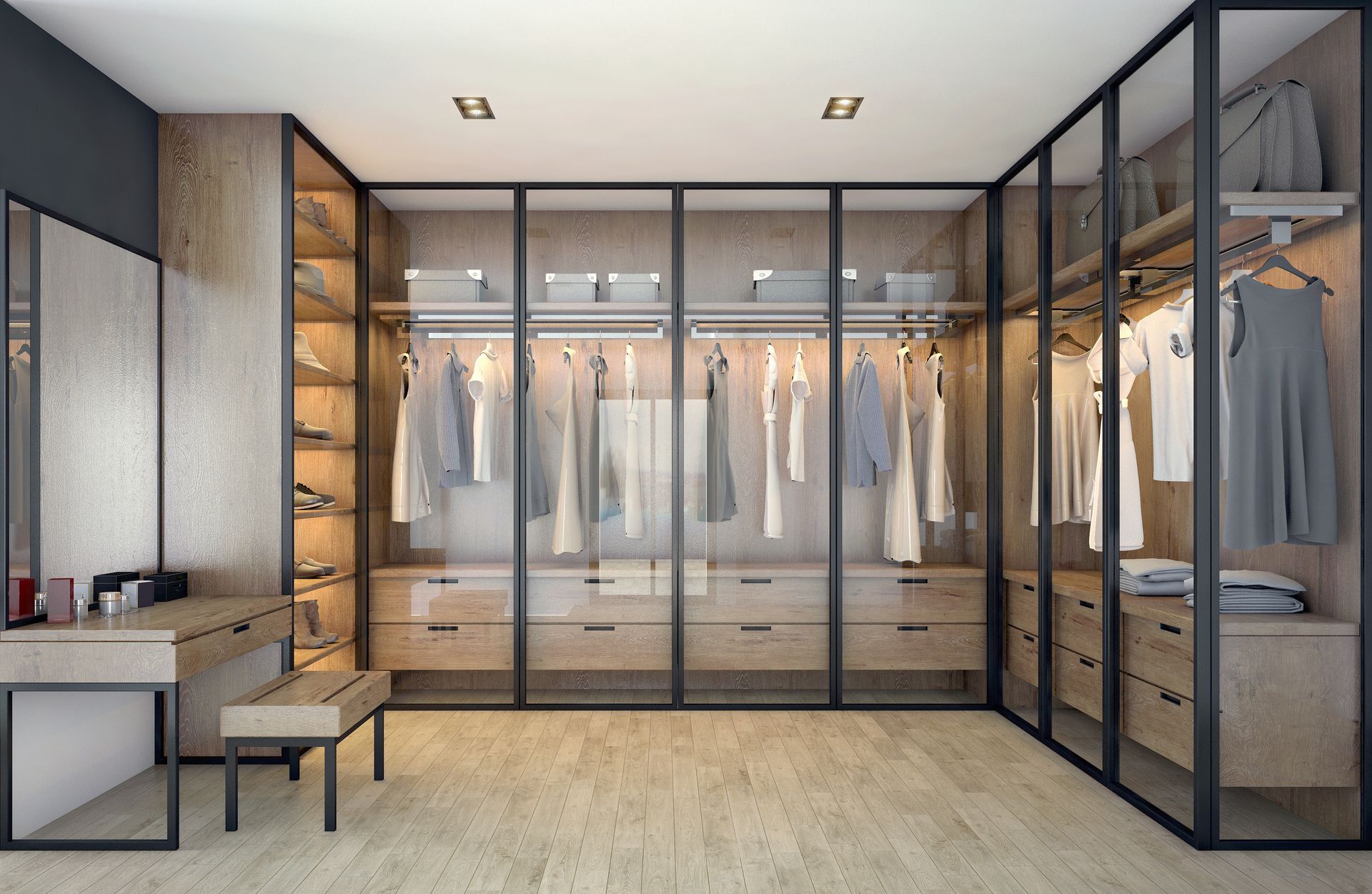 Walk-in closet with glass doors, clothing racks, drawers, and a dressing table. Wooden floors and neutral color palette.