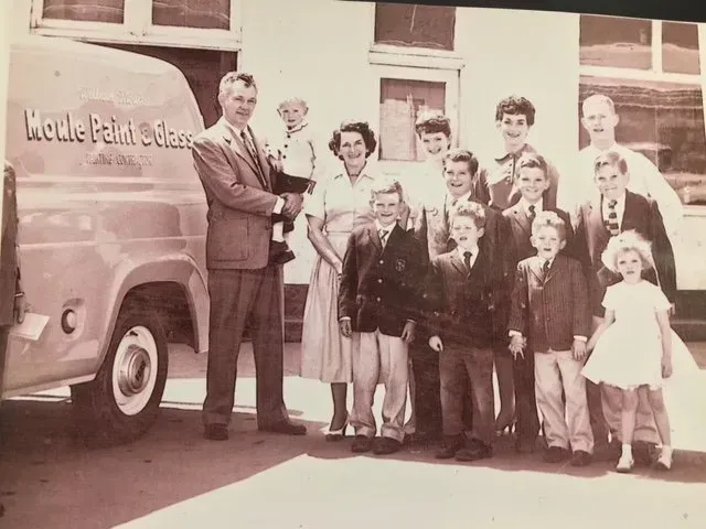 Family poses near a van, likely for a business, outdoors. Adults and children are dressed up, smiling.