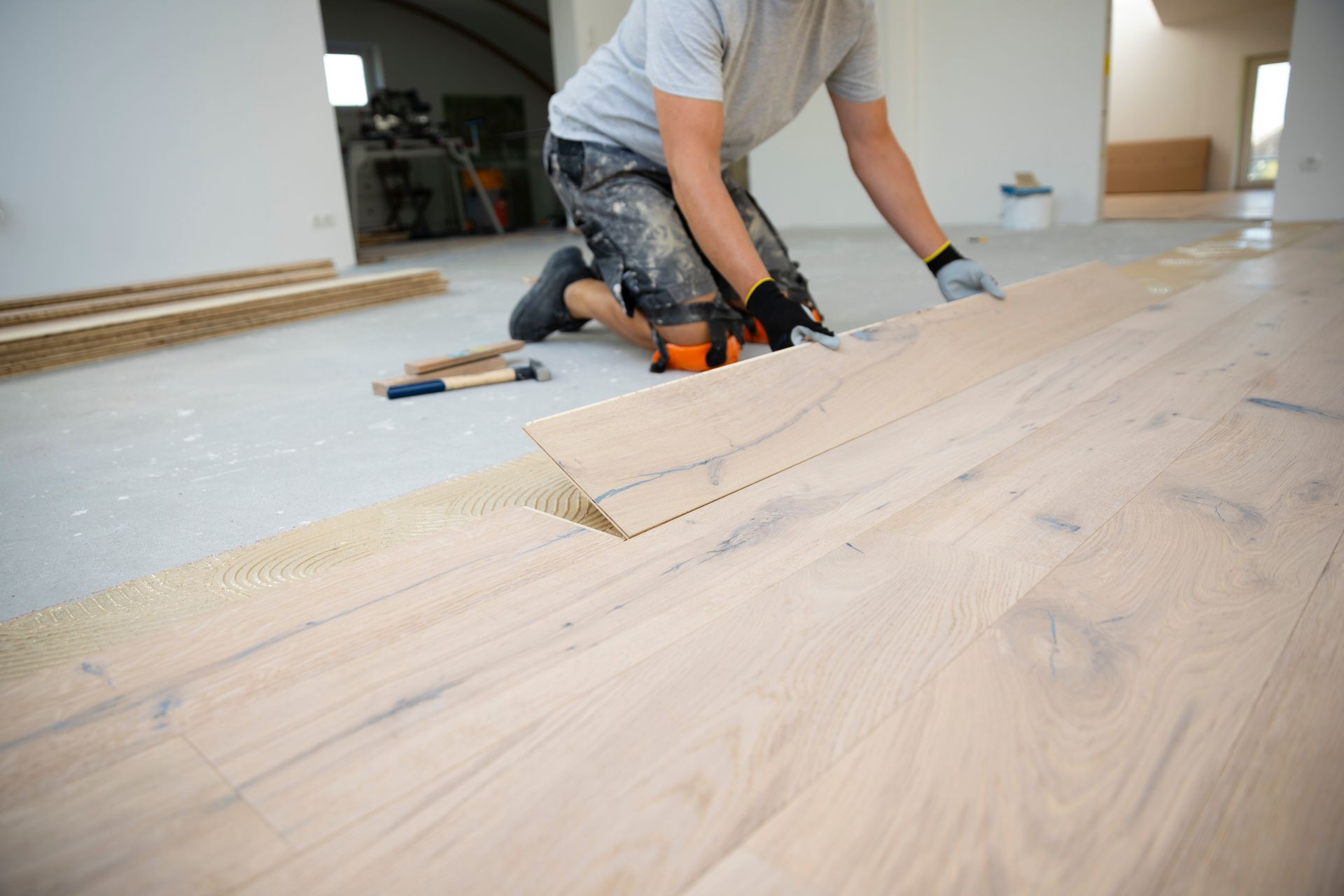 Person installing light-colored wood flooring on a concrete subfloor.