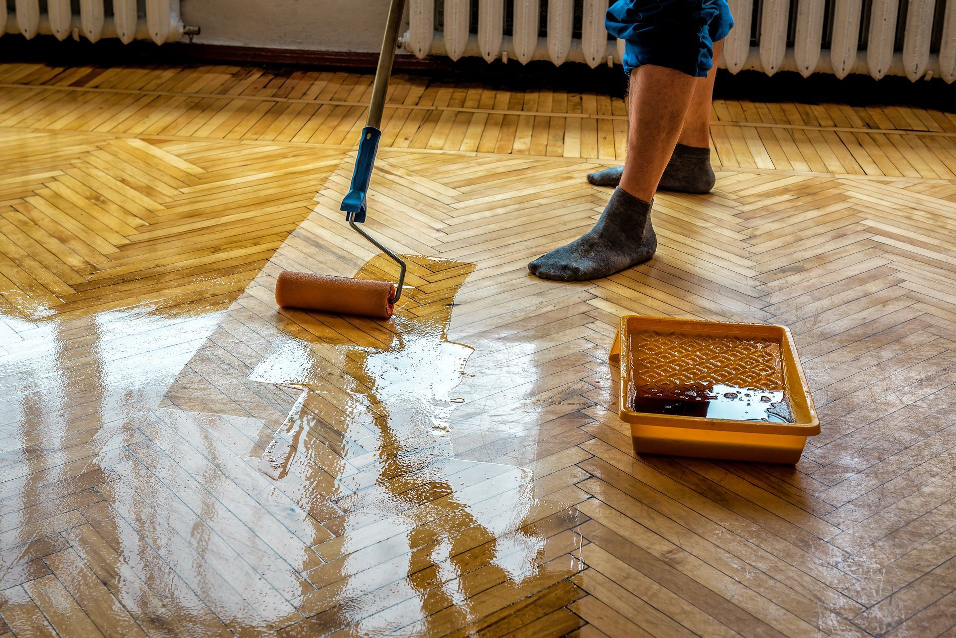 Person applying varnish to wooden parquet floor with a roller.