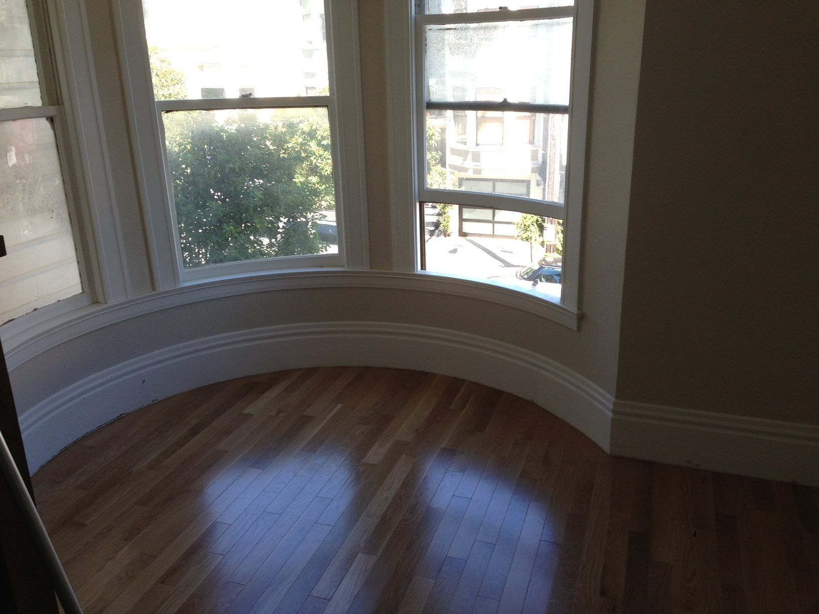 Hardwood floor in a room with a curved bay window and white trim.