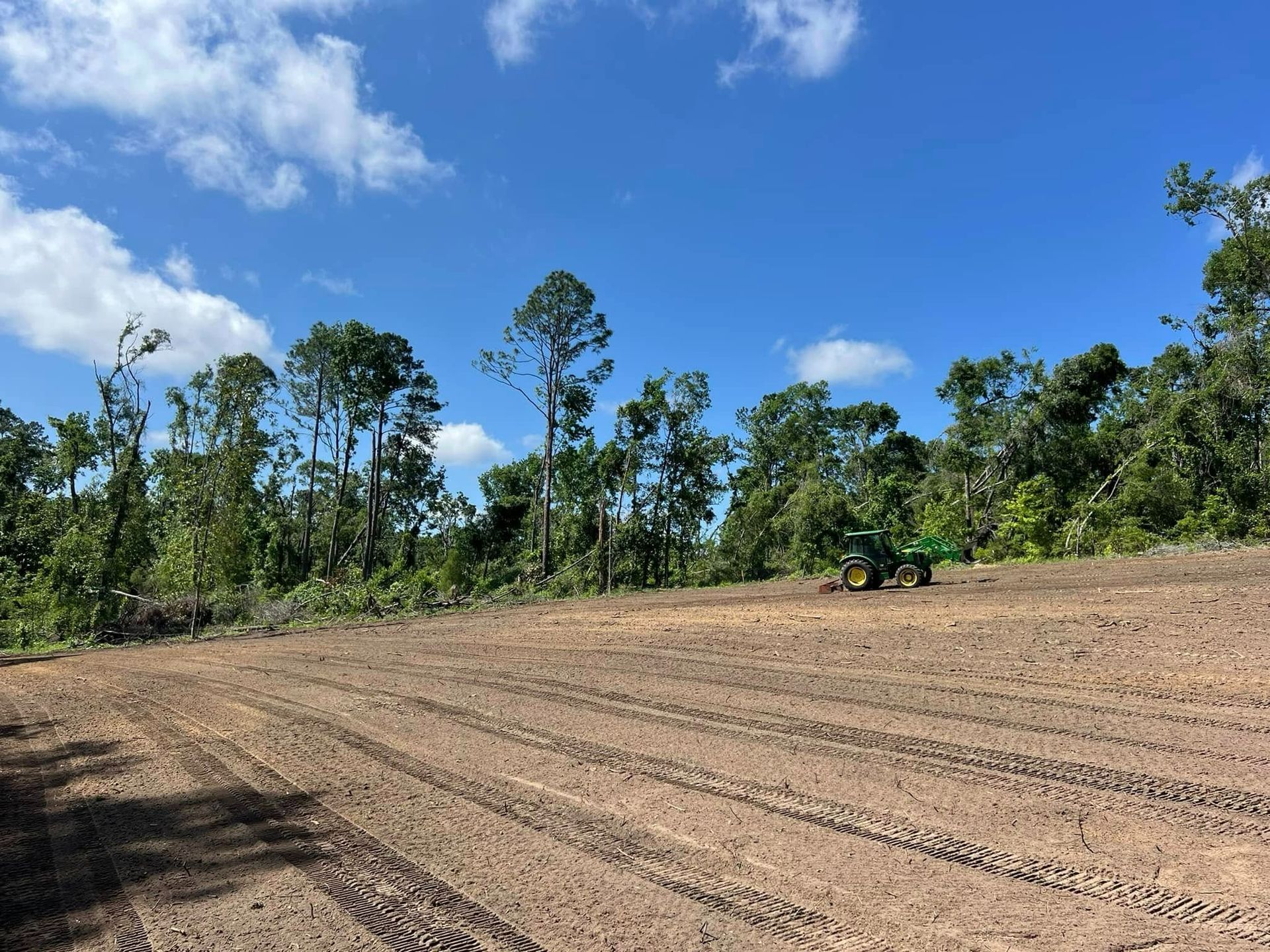 A tractor is plowing a dirt field with trees in the background.