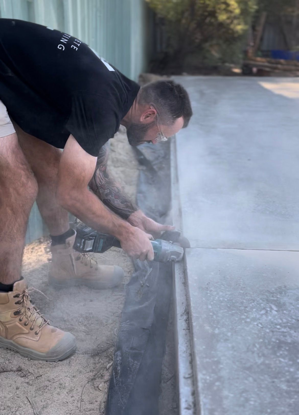 Man using a power saw to cut concrete, sending up dust along a driveway edge — Complete Concreting Riverina In Ashmont, NSW