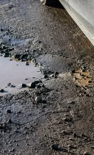 A car is parked on a muddy road next to a puddle of water.