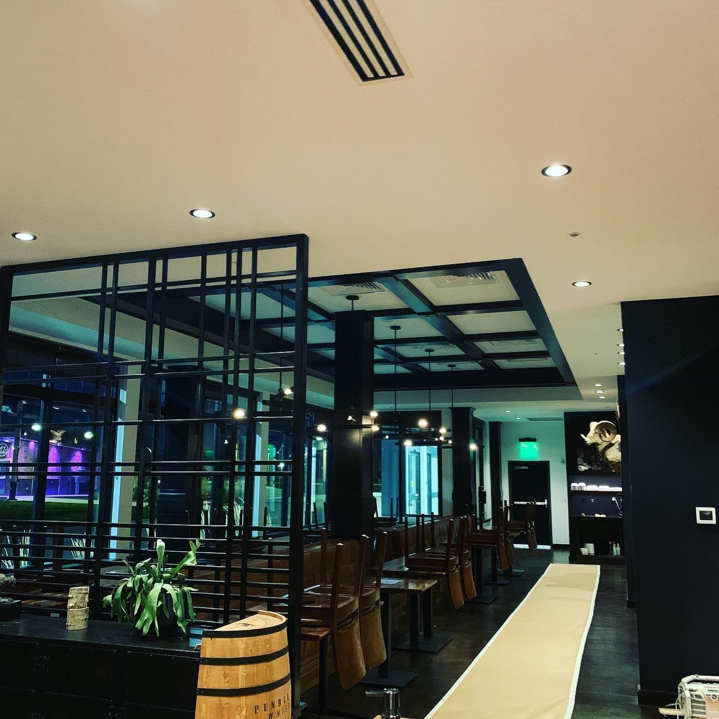 A dimly lit restaurant interior with a black grid partition, wooden chairs, barrel decor, and a white floor runner.