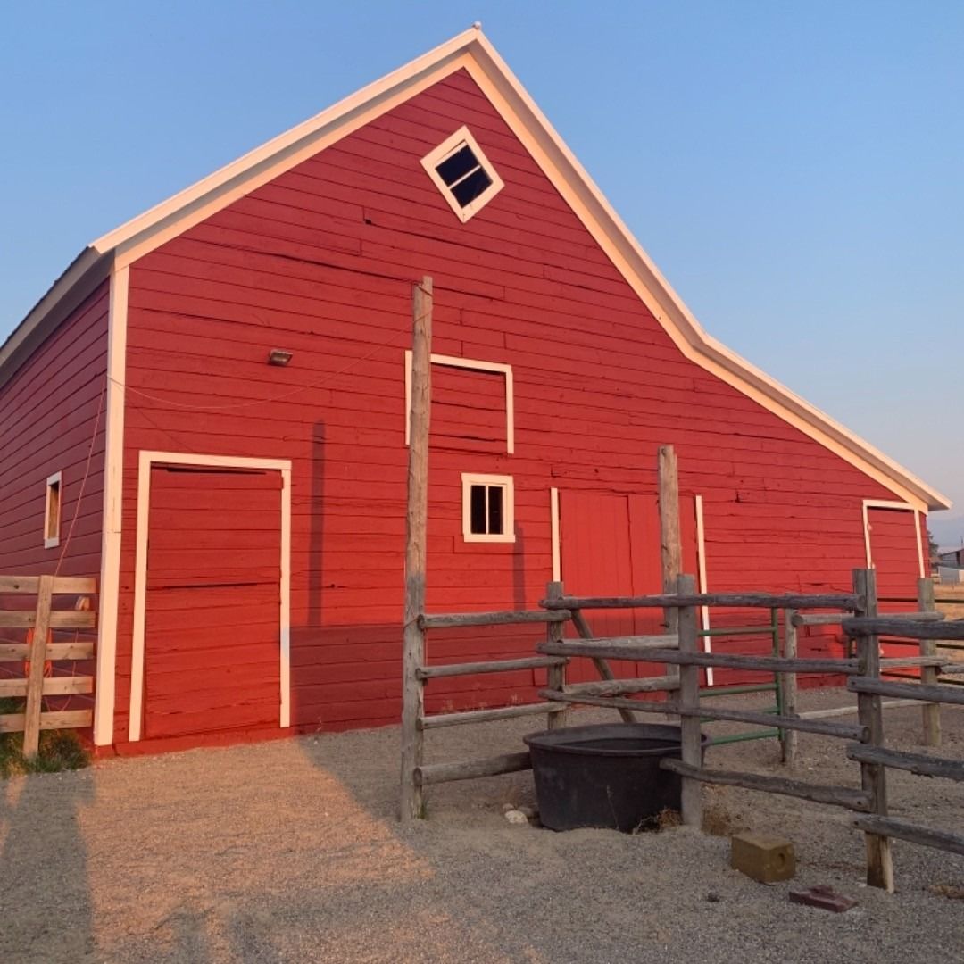 A bright red barn with white trim and a diamond-shaped window, set behind a wooden fence with a dark water trough.