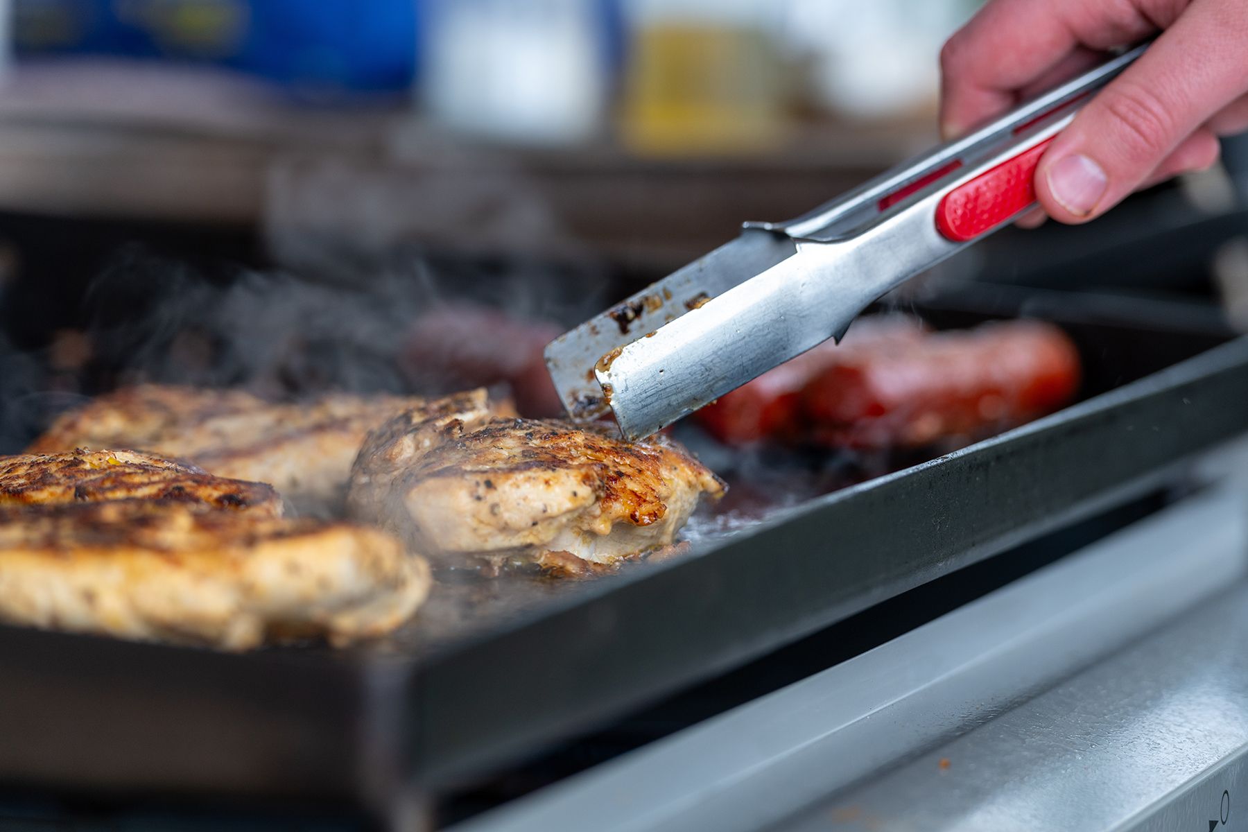 A person is cooking meat on a grill with tongs.
